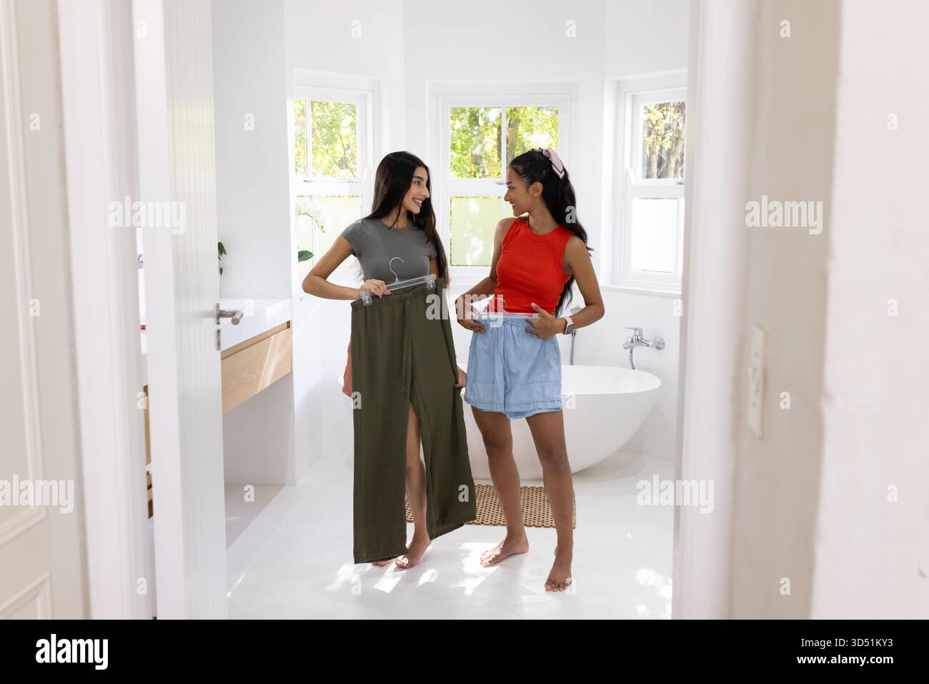 Diverse amiche con gonna verde oliva e pantaloncini blu in bagno, vasca e lavandino Foto Stock