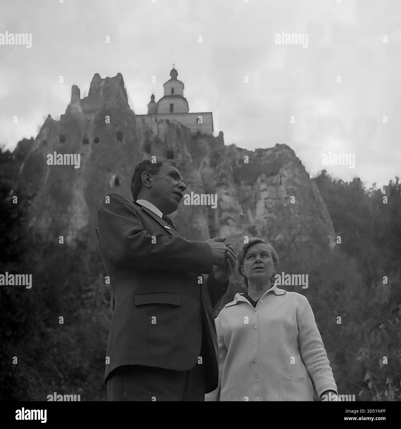 Questa fotografia d'archivio in bianco e nero del 1975 cattura un momento potente e toccante a Sviatohirsk (allora Slavyanogorsk), RSS Ucraina. Il veterano cieco Shutenko, accompagnato da una donna, si erge ai piedi delle enormi e iconiche scogliere di gesso. Si affacciano da un'angolazione bassa sulla storica chiesa di San Nicola, parte della Sovrintendenza dei Monti Santi di Sviatohirsk Lavra, arroccata drammaticamente sulla cima della scogliera. Questa immagine ritrae un momento personale di turismo e riflessione per il veterano della seconda guerra mondiale. Foto Stock
