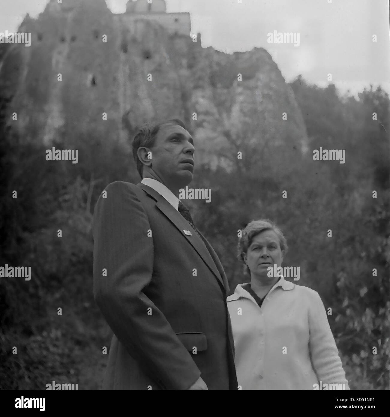 Questa fotografia d'archivio in bianco e nero del 1975 cattura un momento potente e toccante a Sviatohirsk (allora Slavyanogorsk), RSS Ucraina. Il veterano cieco Shutenko, accompagnato da una donna, si erge ai piedi delle enormi e iconiche scogliere di gesso. Si affacciano da un'angolazione bassa sulla storica chiesa di San Nicola, parte della Sovrintendenza dei Monti Santi di Sviatohirsk Lavra, arroccata drammaticamente sulla cima della scogliera. Questa immagine ritrae un momento personale di turismo e riflessione per il veterano della seconda guerra mondiale. Foto Stock