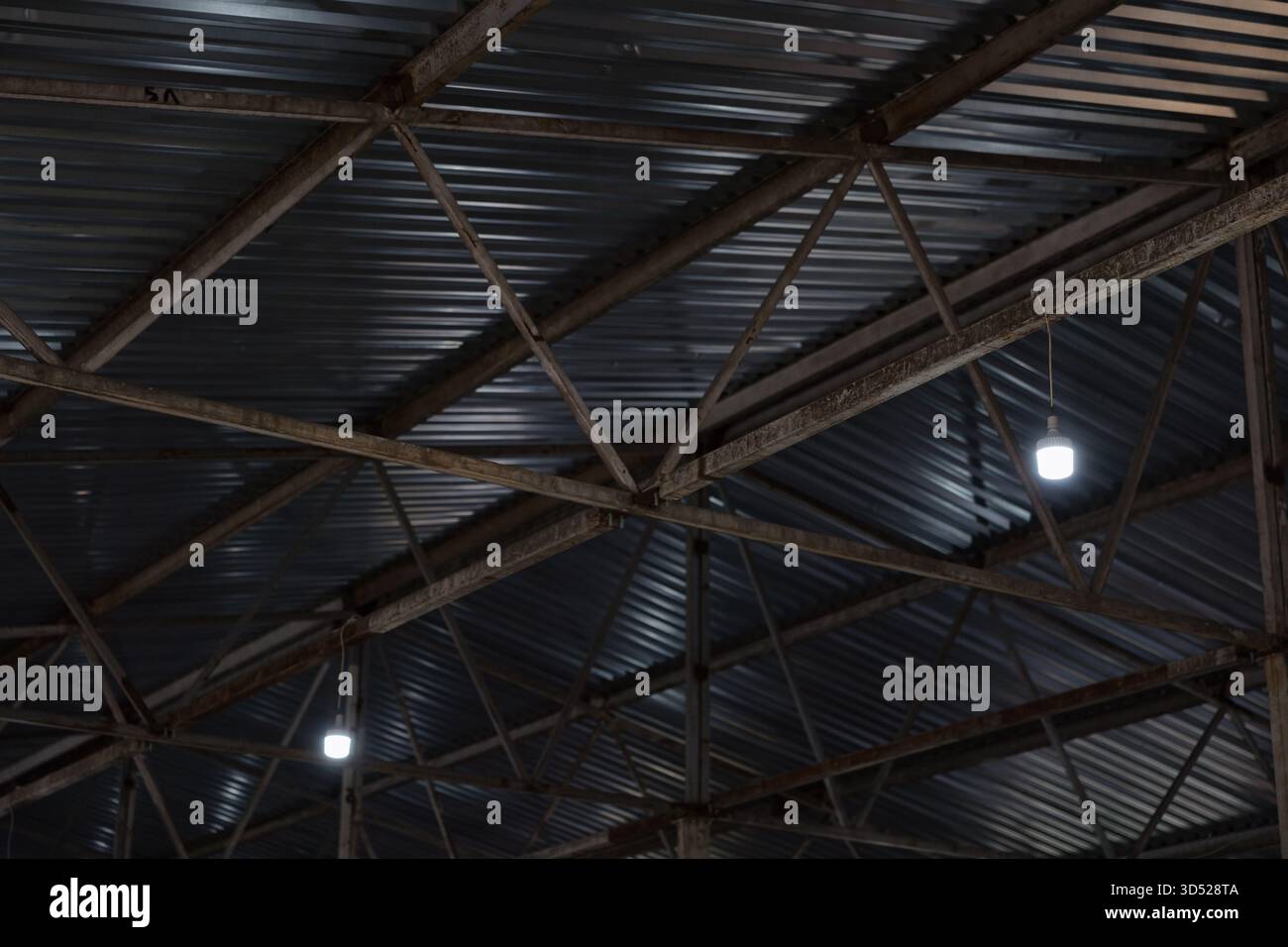 Una vista delle travi a soffitto in uno spazio di produzione incompleto della caldaia mostra le materie prime e gli impianti di illuminazione industriali. Foto Stock