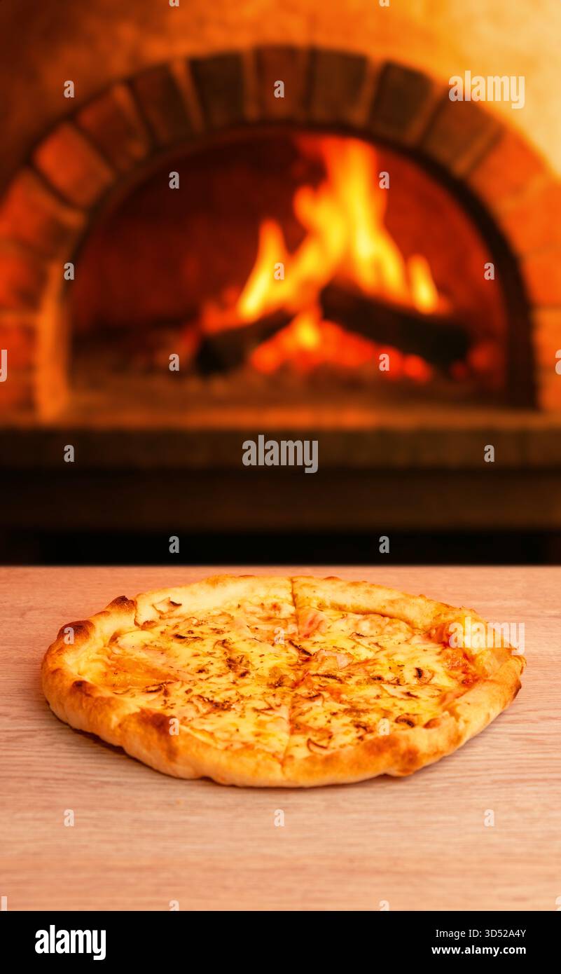 Pizza calda con formaggio fuso davanti ad un forno in mattoni rustico, fuoco caldo che crea un'atmosfera accogliente Foto Stock