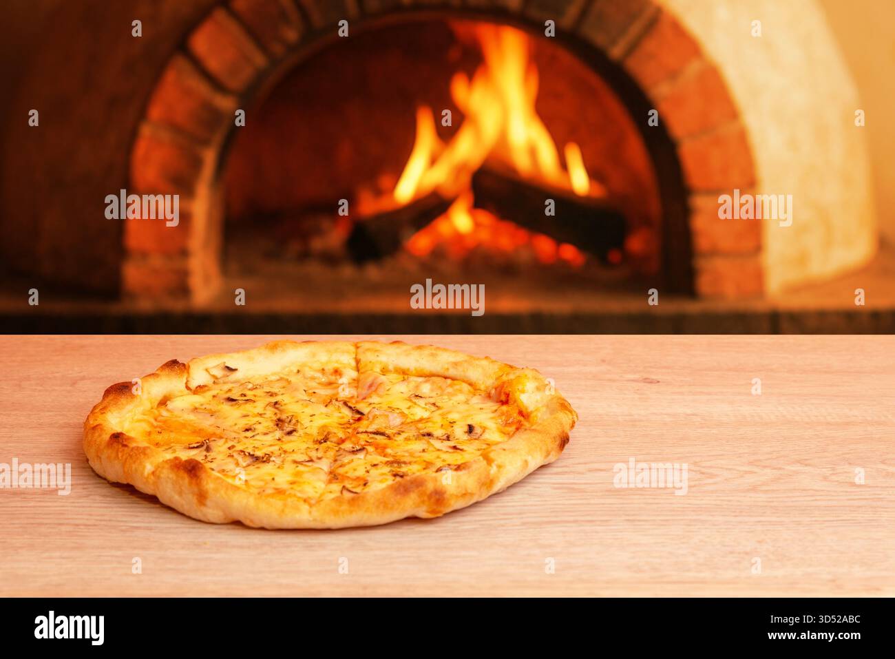 Pizza su tavolo in legno con tradizionale forno in mattoni e fiamme visibili sullo sfondo, atmosfera calda e rustica Foto Stock