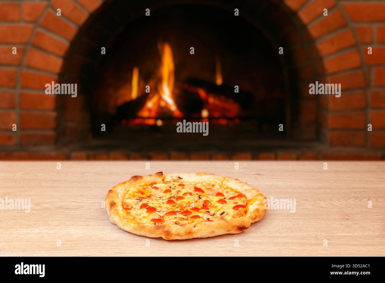 Pizza calda con formaggio fuso e salsa di pomodoro servita su un tavolo di legno di fronte al rustico forno in mattoni con fiamme libere Foto Stock