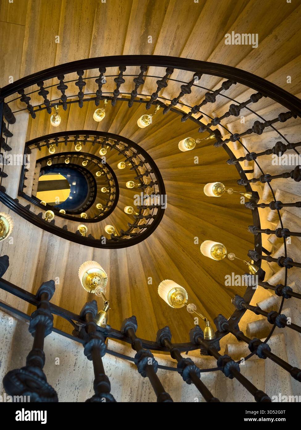 Scala a chiocciola catturata dall'alto che mostra ringhiere di ferro ornamentali la calda luce delle lampade rotonde crea un motivo geometrico che invita a un'atmosfera cinematografica e un'architettura spettacolare. Foto Stock