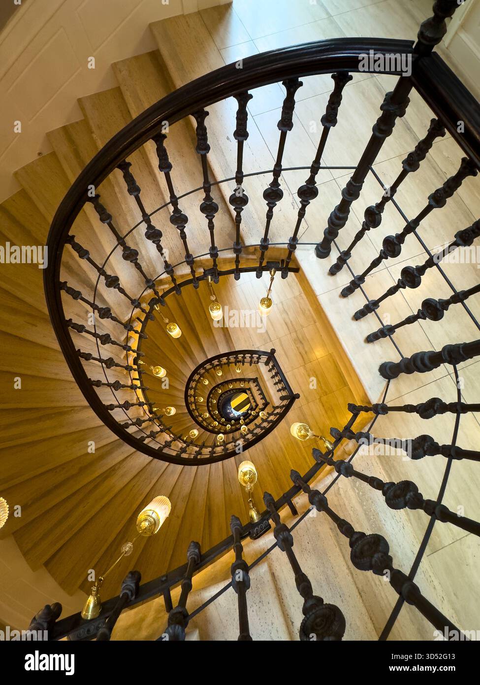 Scalinata a spirale dall'alto con balaustre in ferro scuro e luci a sospensione che creano curve spettacolari e un'atmosfera calda Foto Stock