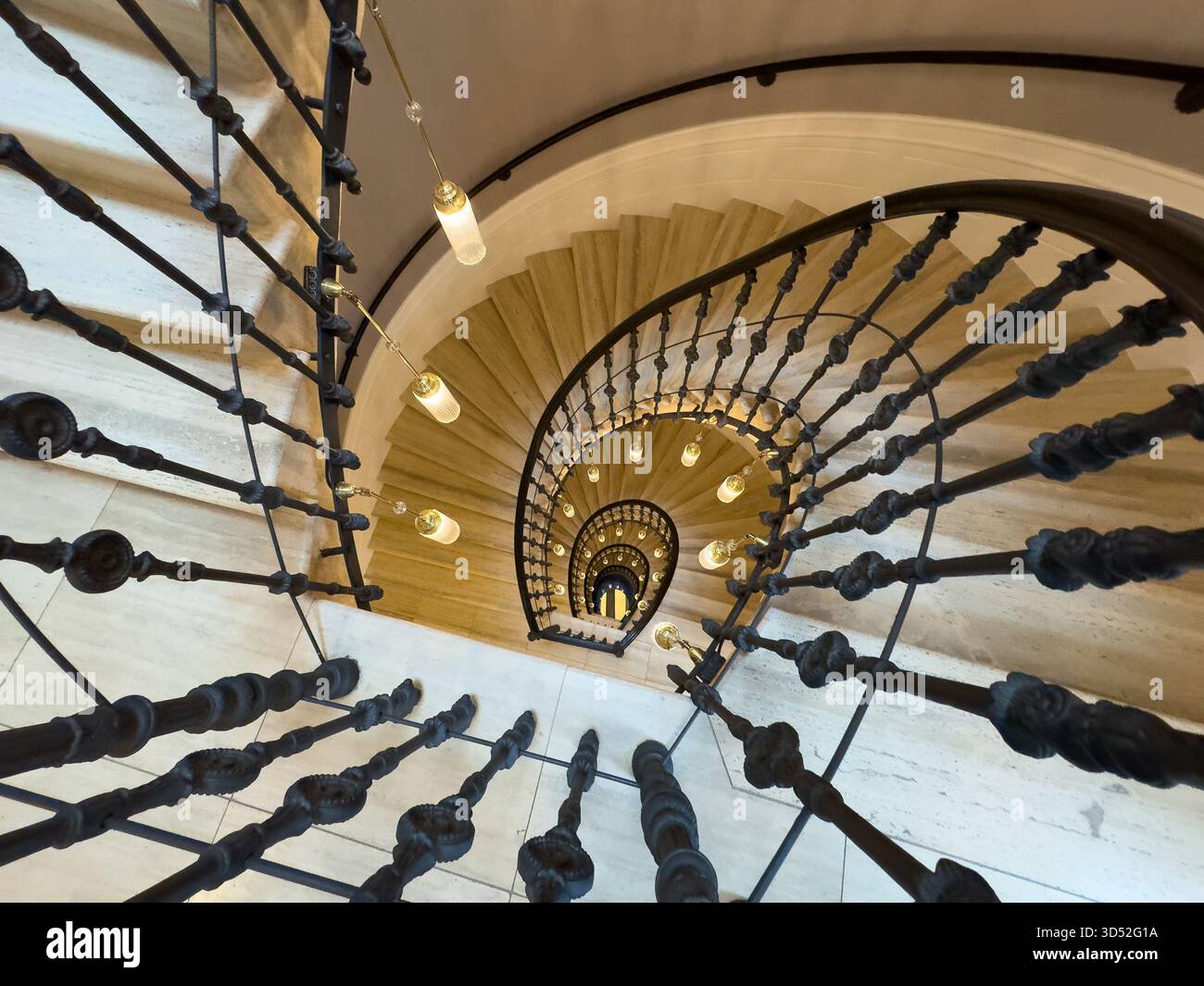 Scalinata a spirale dall'alto con ringhiera curva, calde luci a sospensione gradini in pietra creano profondità ed eleganza nell'atmosfera architettonica degli interni Foto Stock