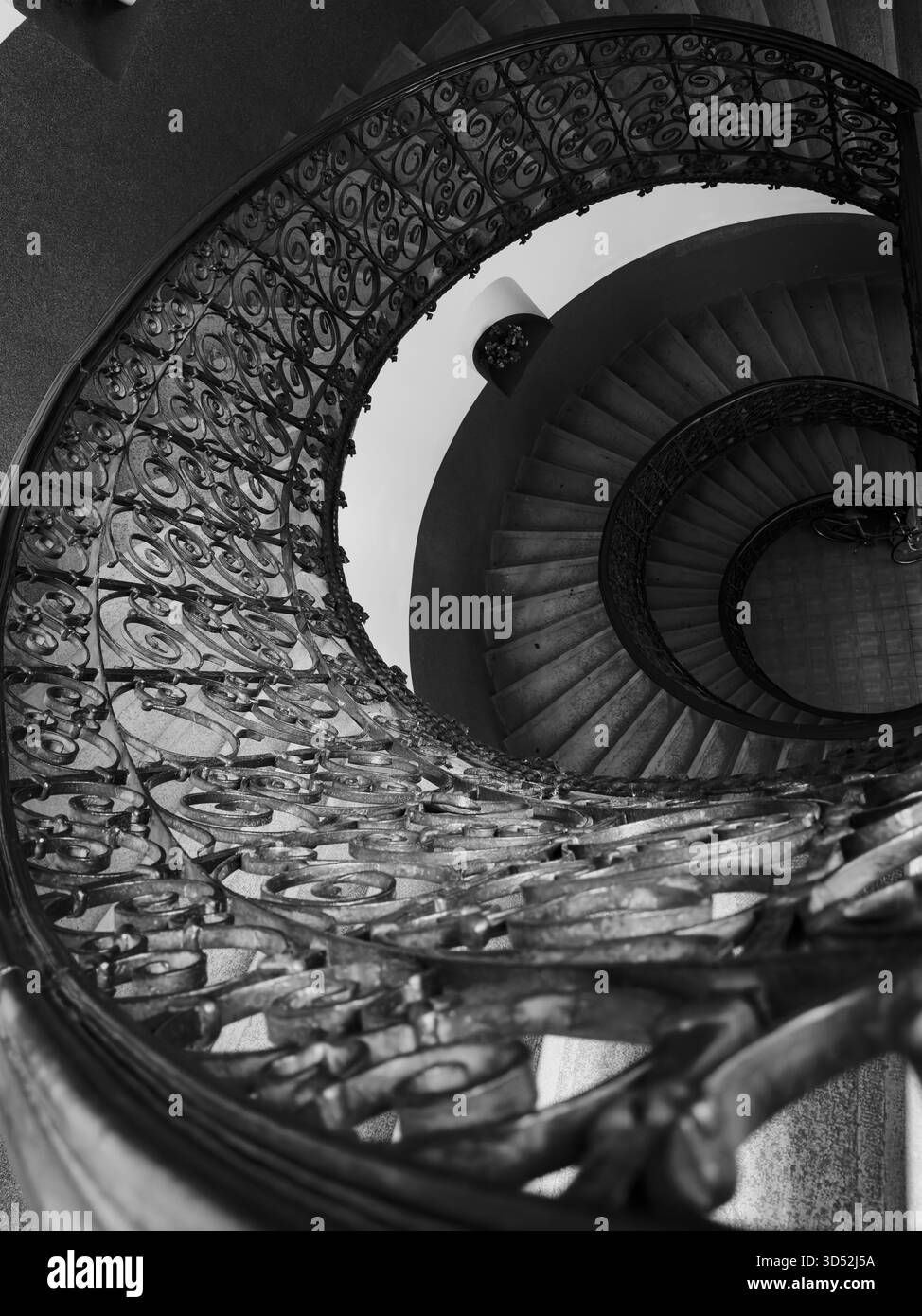 La vista dall'alto della scala a chiocciola monocromatica mostra i gradini decorativi in ferro che creano profondità e simmetria drammatiche Foto Stock