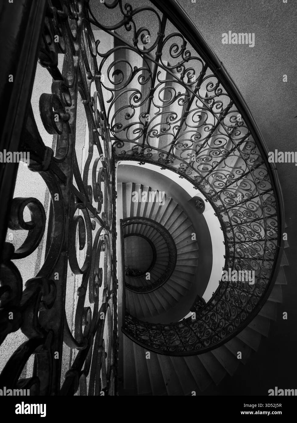 La scala a chiocciola bianca e nera rivela ringhiere ornate in ferro battuto design curvo prospettiva di profondità in eleganti interni architettonici Foto Stock