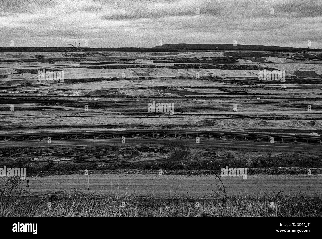 Garzweiler, Tagebau. La miniera di carbone marrone a cielo aperto di Garzweiler Tagebau sta diventando sempre più grande entro la settimana, estraendo combustibili fossili come la lignite e il carbone marrone che alimentano la vicina centrale elettrica di Garzweiler Kraftwerk e produce enormi quantità di gas serra come carbonio e CO2, contribuendo così al riscaldamento globale e ai cambiamenti climatici. Nordrhine-Westfalia, Germania. Girato su Analog Black & White Film, 2024. Garzweiler Garzweiler Tagebau Nordrhein-Westfalen Germania Copyright: XGuidoxKoppesxPhotox Foto Stock