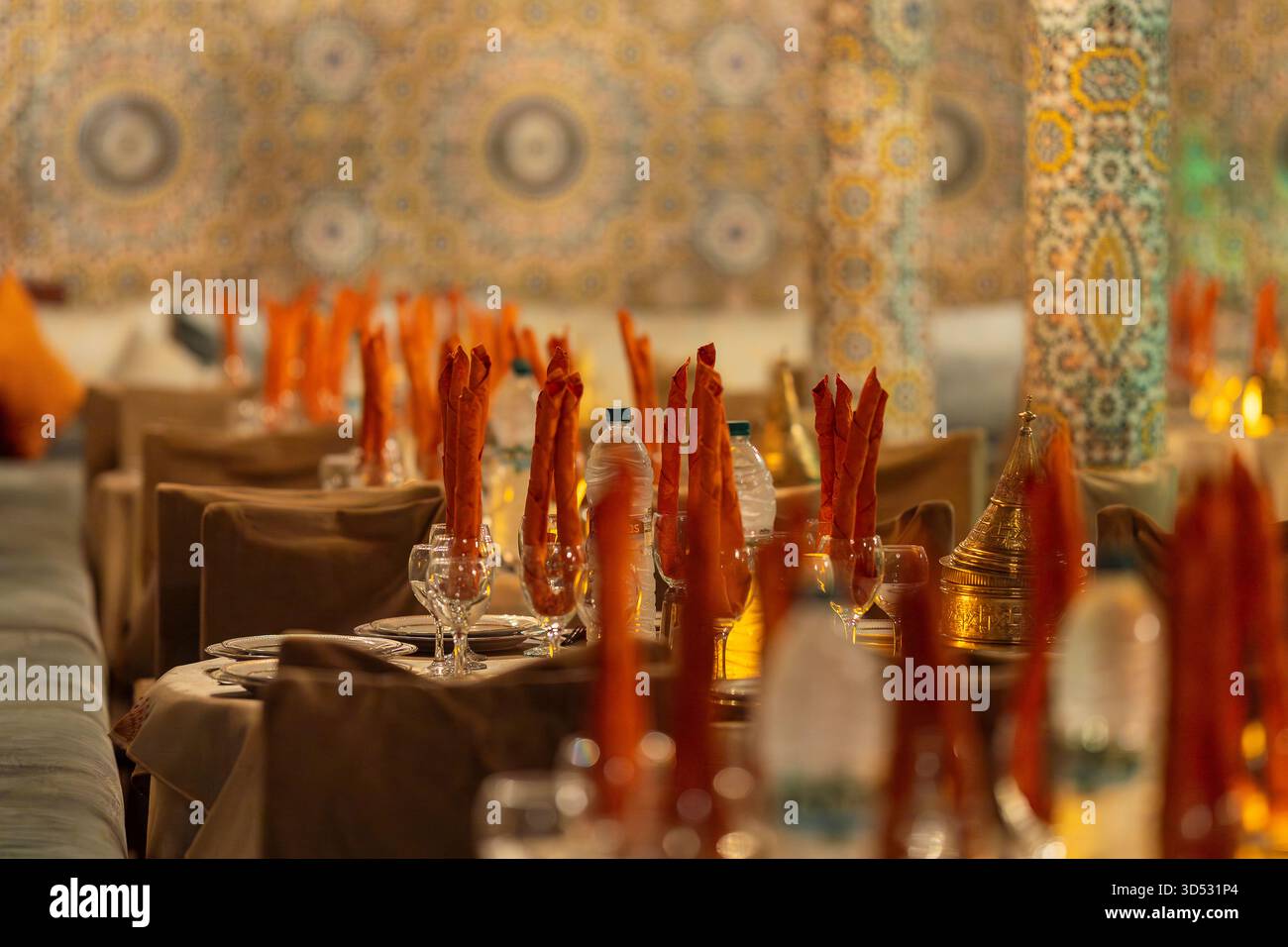 Elegante ambiente da tavolo in un tradizionale ristorante marocchino con colonne piastrellate ornate e luce calda. Sala da pranzo decorata a Marrakech. Foto Stock