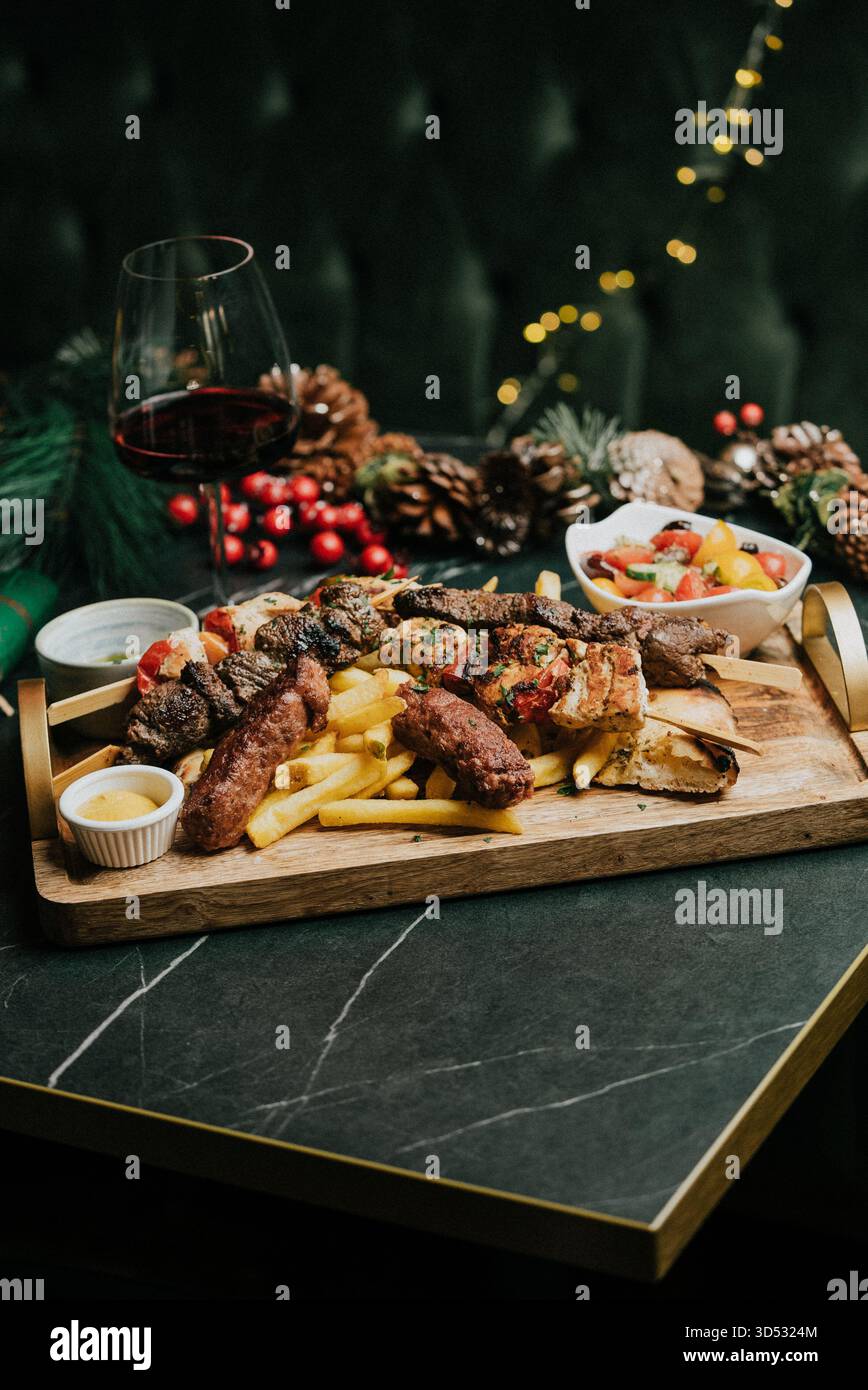 Un vassoio di cibo con un bicchiere di vino su un tavolo. Il cibo include carne, patate e verdure. Il bicchiere di vino è mezzo pieno. La scena è festosa e ce Foto Stock