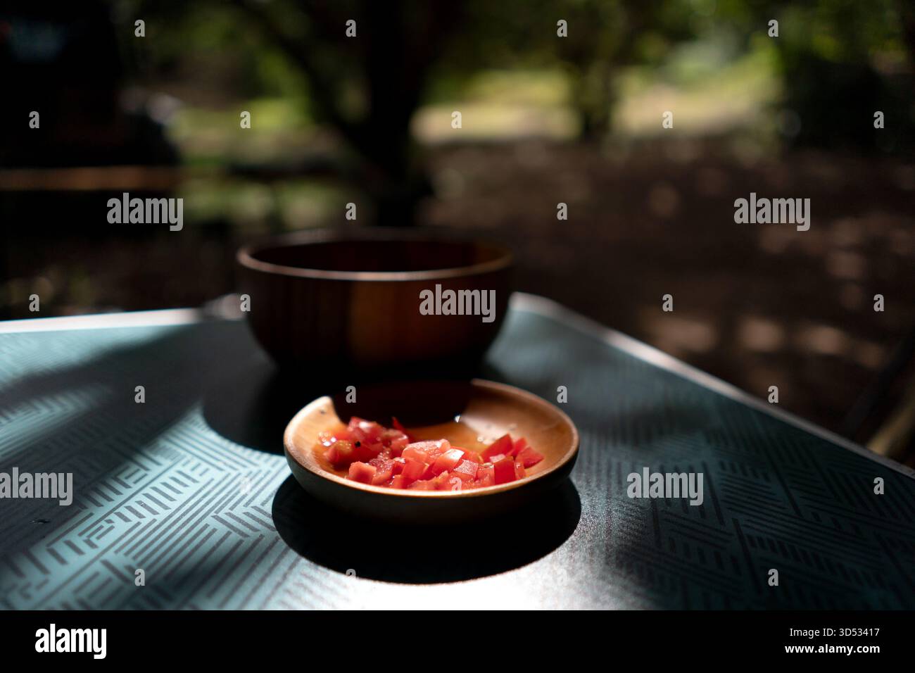 I pomodori freschi vengono tagliati a dadini in una ciotola di legno su un tavolo sotto la luce del sole, creando un'atmosfera rustica da cucina all'aperto. Foto Stock