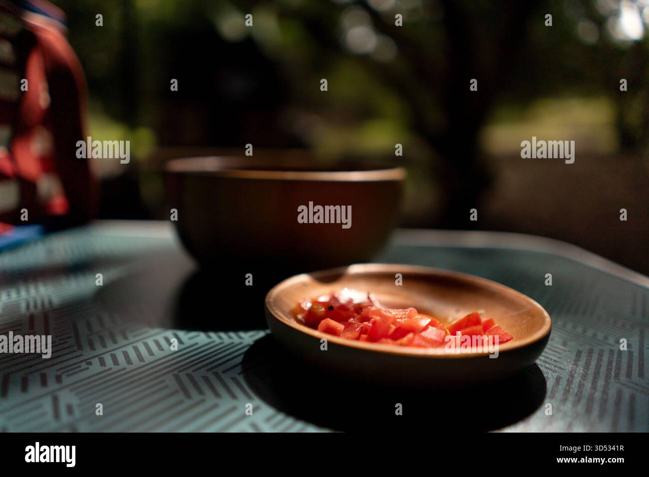 I pomodori freschi vengono tagliati a dadini in una ciotola di legno su un tavolo sotto la luce del sole, creando un'atmosfera rustica da cucina all'aperto. Foto Stock