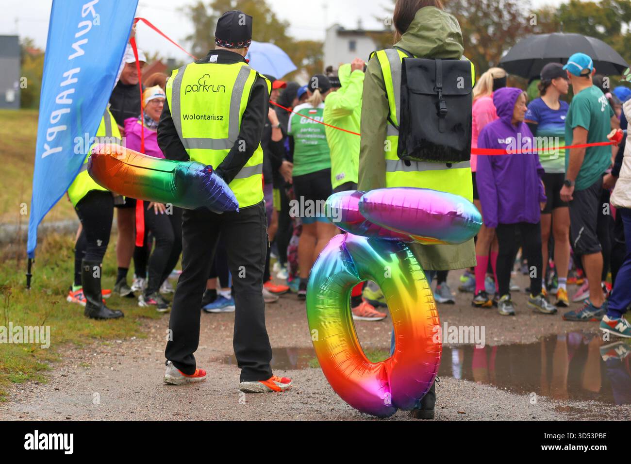 Volontari e partecipanti si riuniscono all'inizio di un evento di parkrun con palloncini colorati. Foto Stock