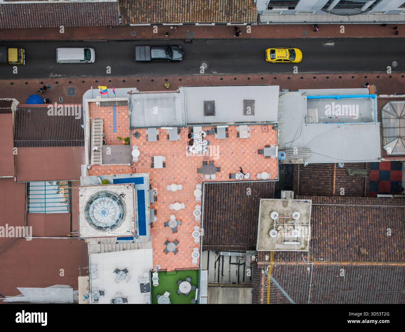Vista aerea di una terrazza sul tetto con pavimento piastrellato, tavoli, sedie e una piscina, in contrasto con il paesaggio urbano circostante, Quito, Ecuador. Foto Stock