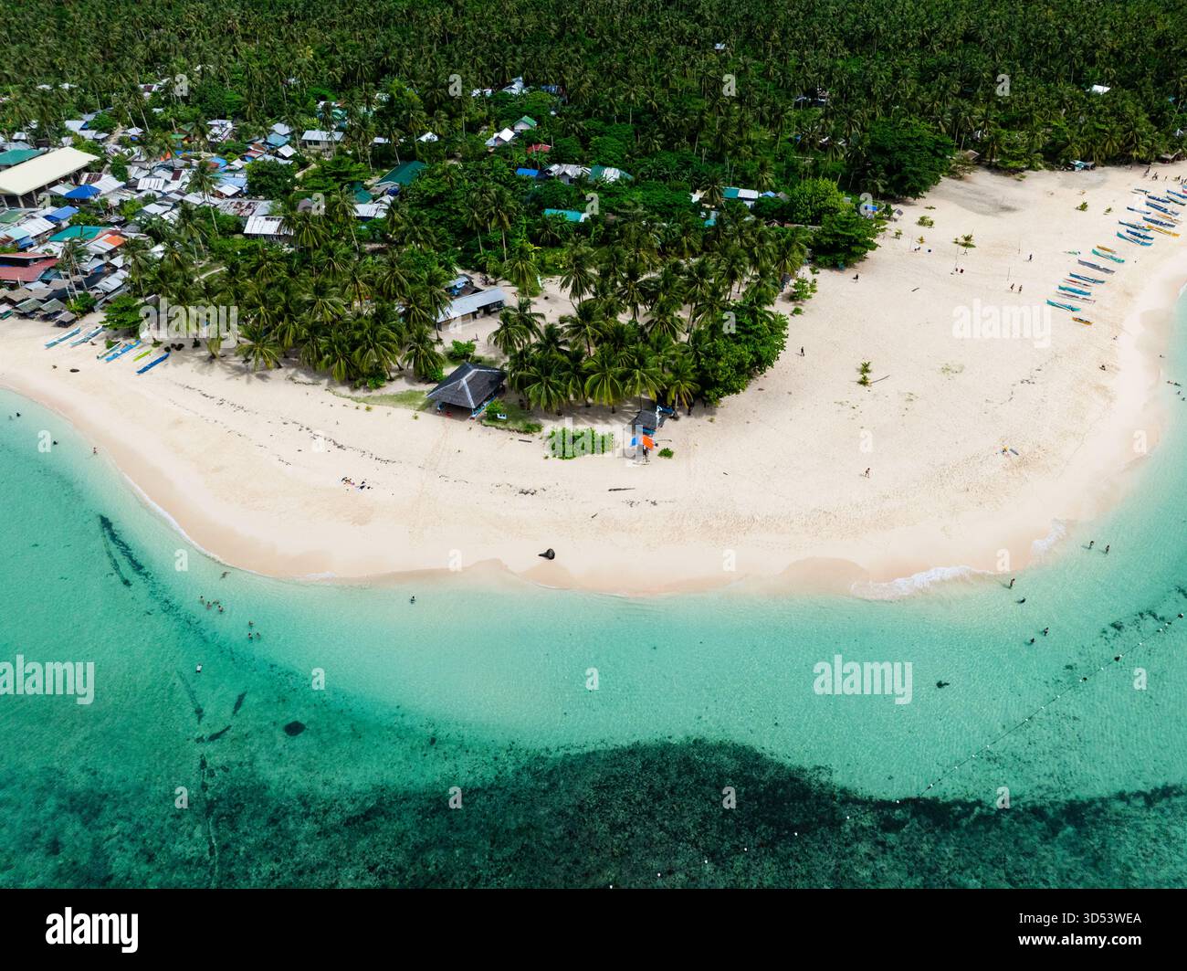 Vista dall'alto della spiaggia con palme e case lungo il litorale accanto all'acqua turchese e alla costa di sabbia chiara. Isola di Daku. Siargao, Filippine. Foto Stock