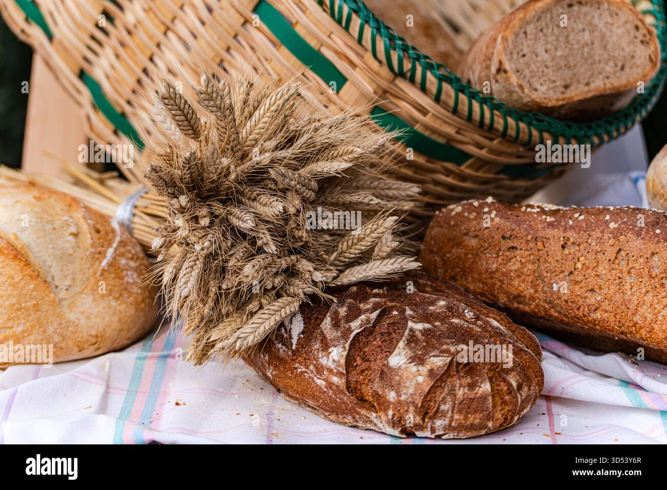 Primo piano di pane assortito su un tavolo con orecchie di grano e cesto in un mercato di strada Foto Stock