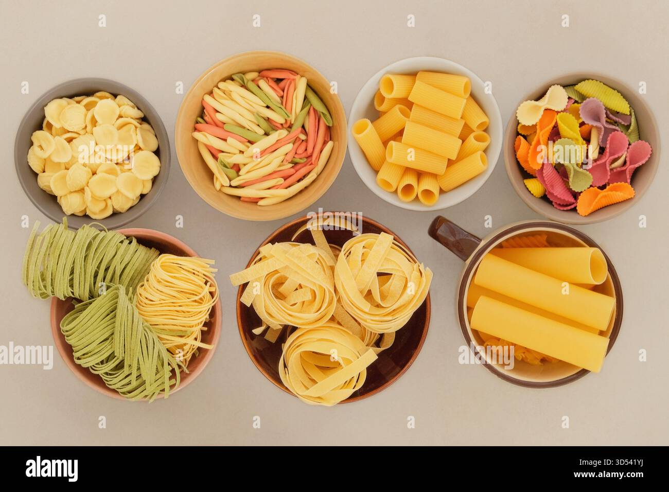 Vista dall'alto. Varietà di pasta multicolore. Set di pasta cruda in ciotole su sfondo chiaro. Conservazione di diversi tipi di pasta secca a casa. Foto Stock