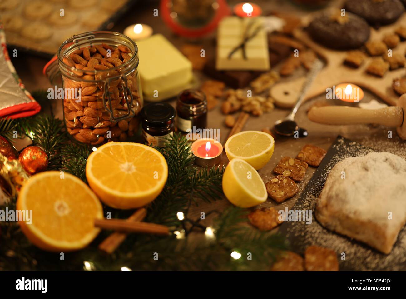 Cottura natalizia con biscotti fatti in casa, arance, noci e lume di candela natalizio su un rustico tavolo in legno. Foto Stock