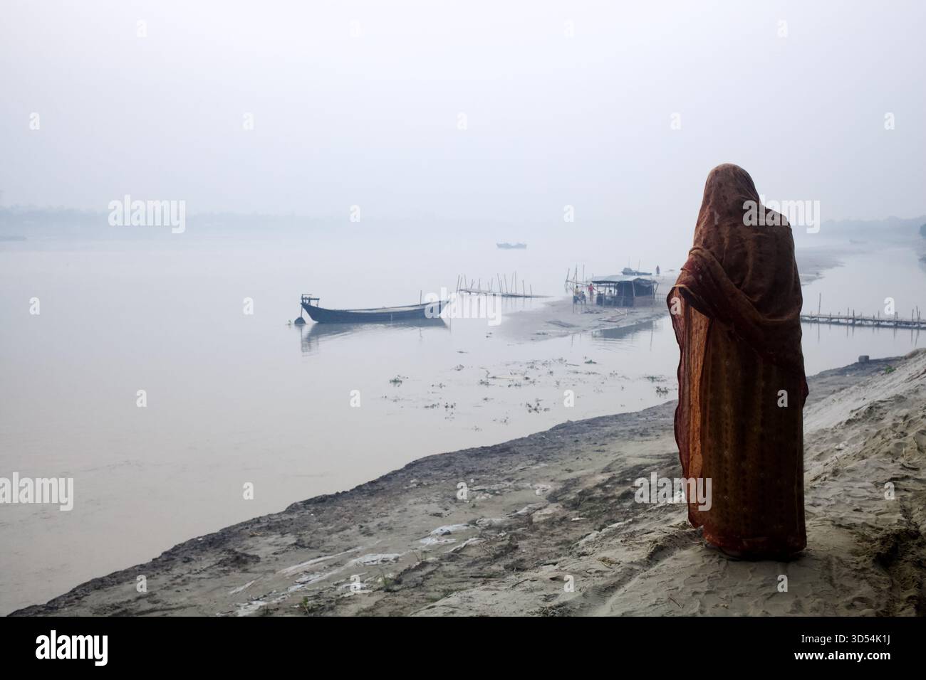 Donna in piedi sulla riva del fiume Madhumati che si affaccia sul pontile Gattia-Kushtia in morbida foschia mattutina, Kuthibari Road, Kushtia, Bangladesh Foto Stock