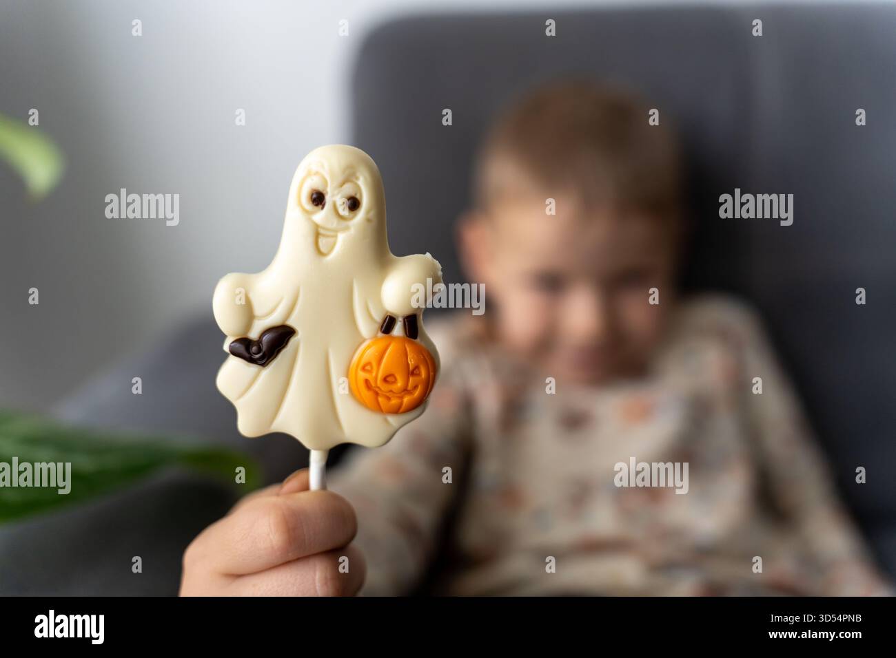 Il bambino tiene in mano un lecca lecca-lecca fantasma al cioccolato bianco con decorazione di zucca arancione mentre il ragazzo sfocato sullo sfondo attende una delizia. Concetto di "Halloween cele" Foto Stock
