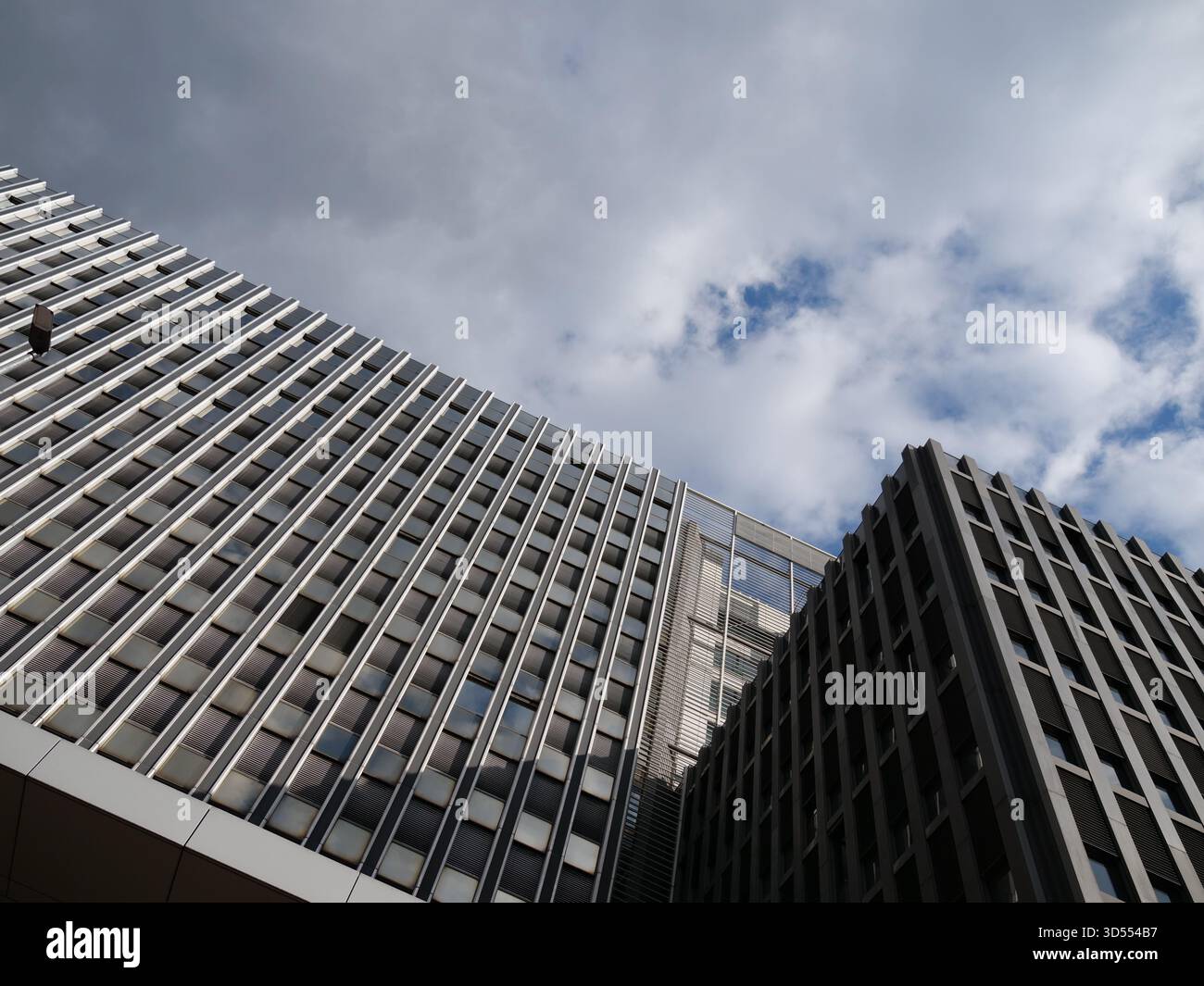 Vista ad angolo basso della facciata di un moderno edificio di uffici con ripetitive alette verticali in metallo e finestre riflettenti in vetro sotto un cielo nuvoloso. Ideale per arcuiti Foto Stock