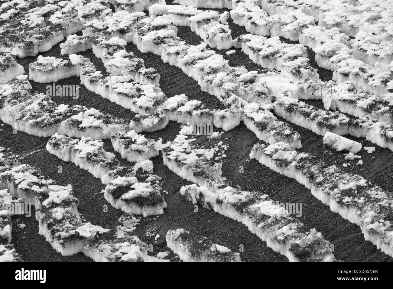 Sfondo a trama astratta, neve bianca incrinata su sabbia nera Foto Stock
