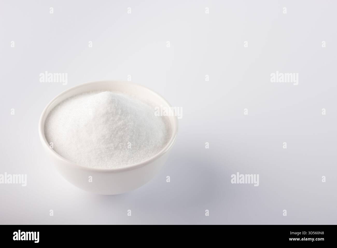 Una ciotola contiene un mucchio di zucchero bianco finissimo, appoggiato su una superficie leggera. Questo semplice ingrediente è essenziale per vari dessert e ricette di cucina. Foto Stock