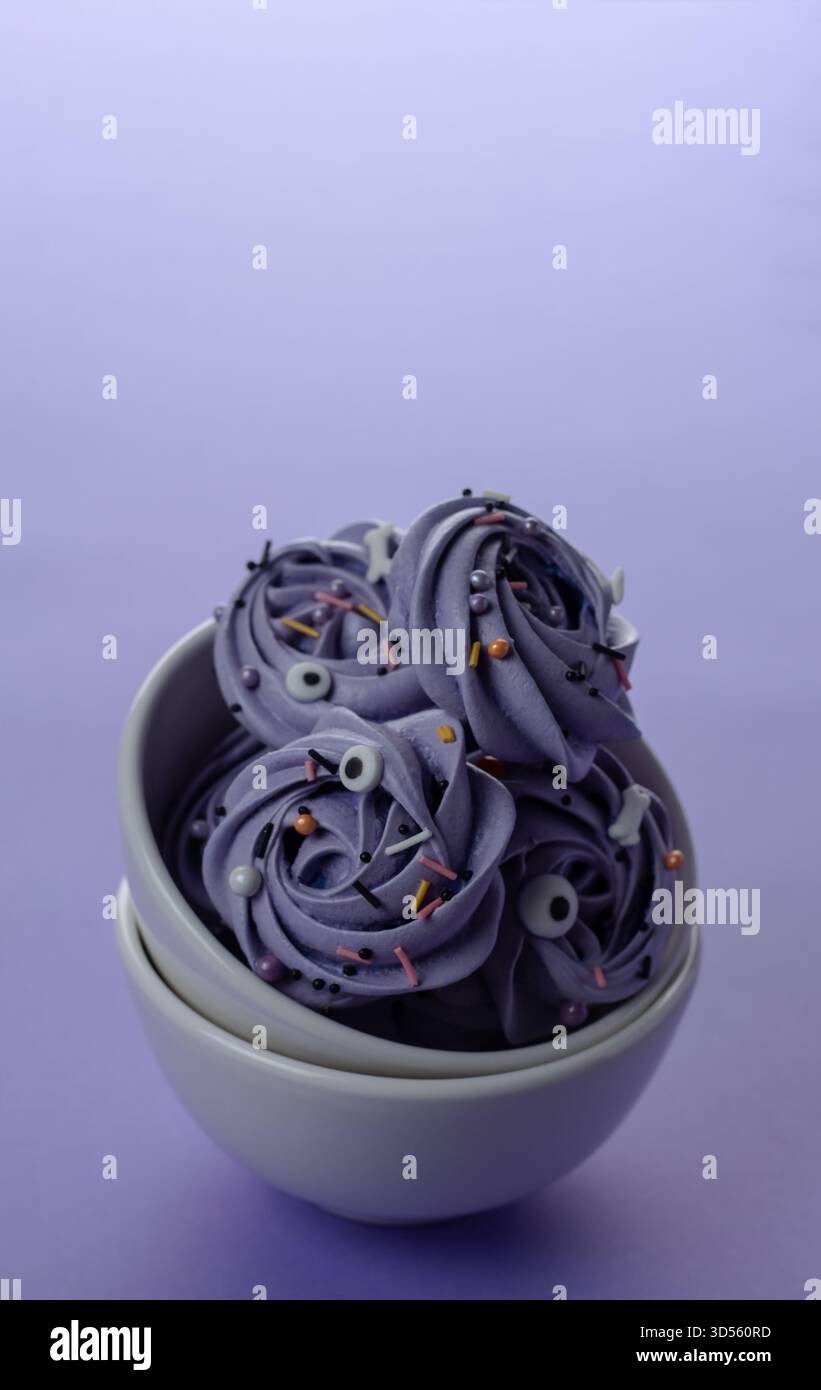 I deliziosi vortici viola per dessert sono disposti artisticamente in una ciotola grigia. Gli spruzzi luminosi aggiungono un tocco di colore al morbido sfondo viola Foto Stock