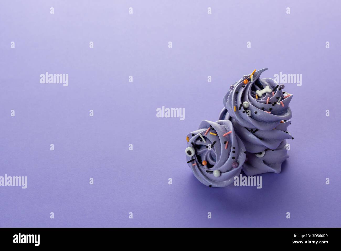 Due eleganti rotoli di glassa alla lavanda si trovano su una superficie liscia color viola pastello, decorata con vivaci spruzzi. Foto Stock