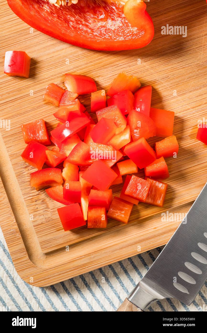 Peperoni rossi rossi rossi a dadini organici su un tagliere Foto Stock