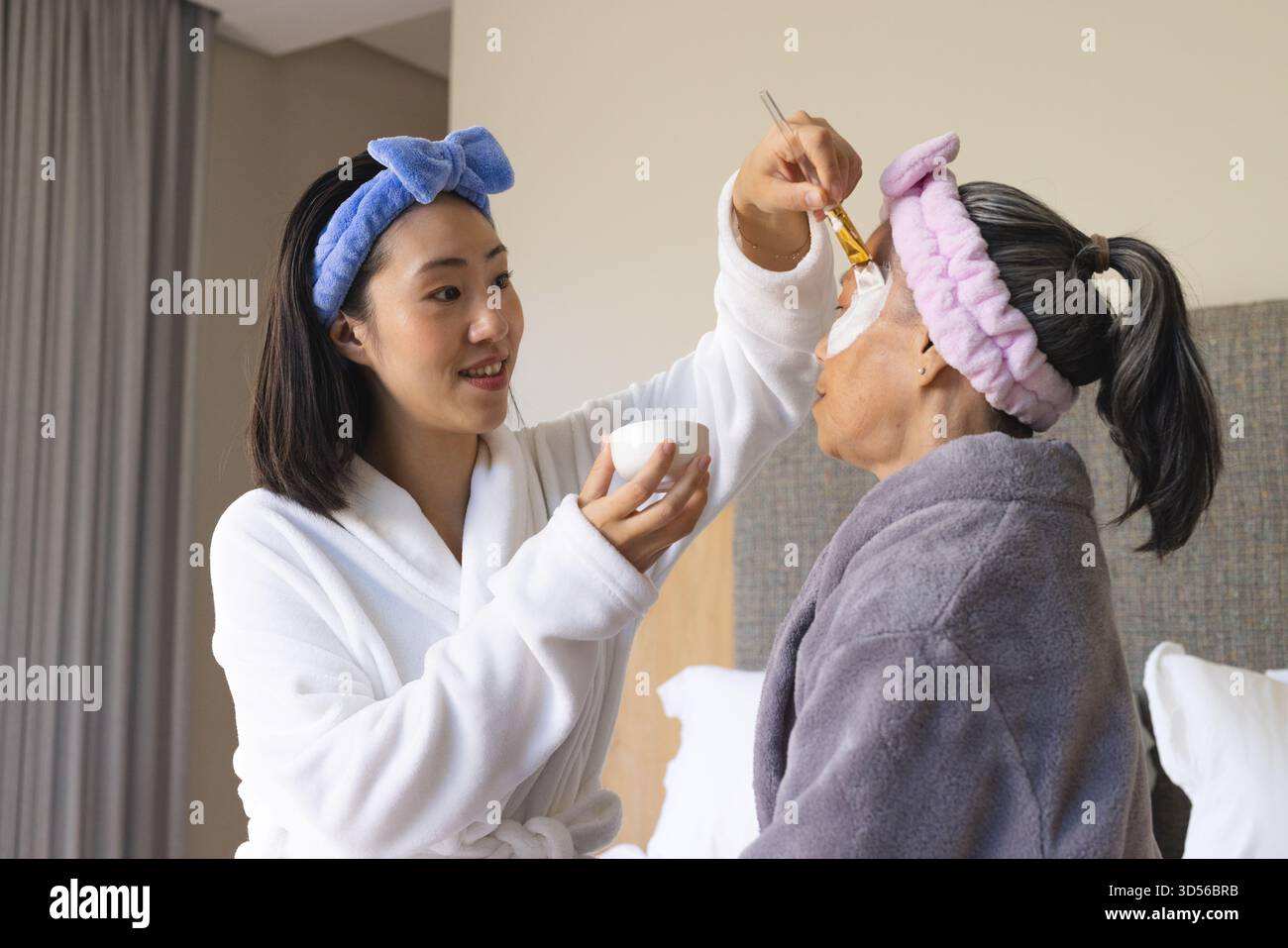 Applicazione della maschera facciale asiatica madre e figlia cinese con spazzola in camera da letto, con ciotola in ceramica Foto Stock