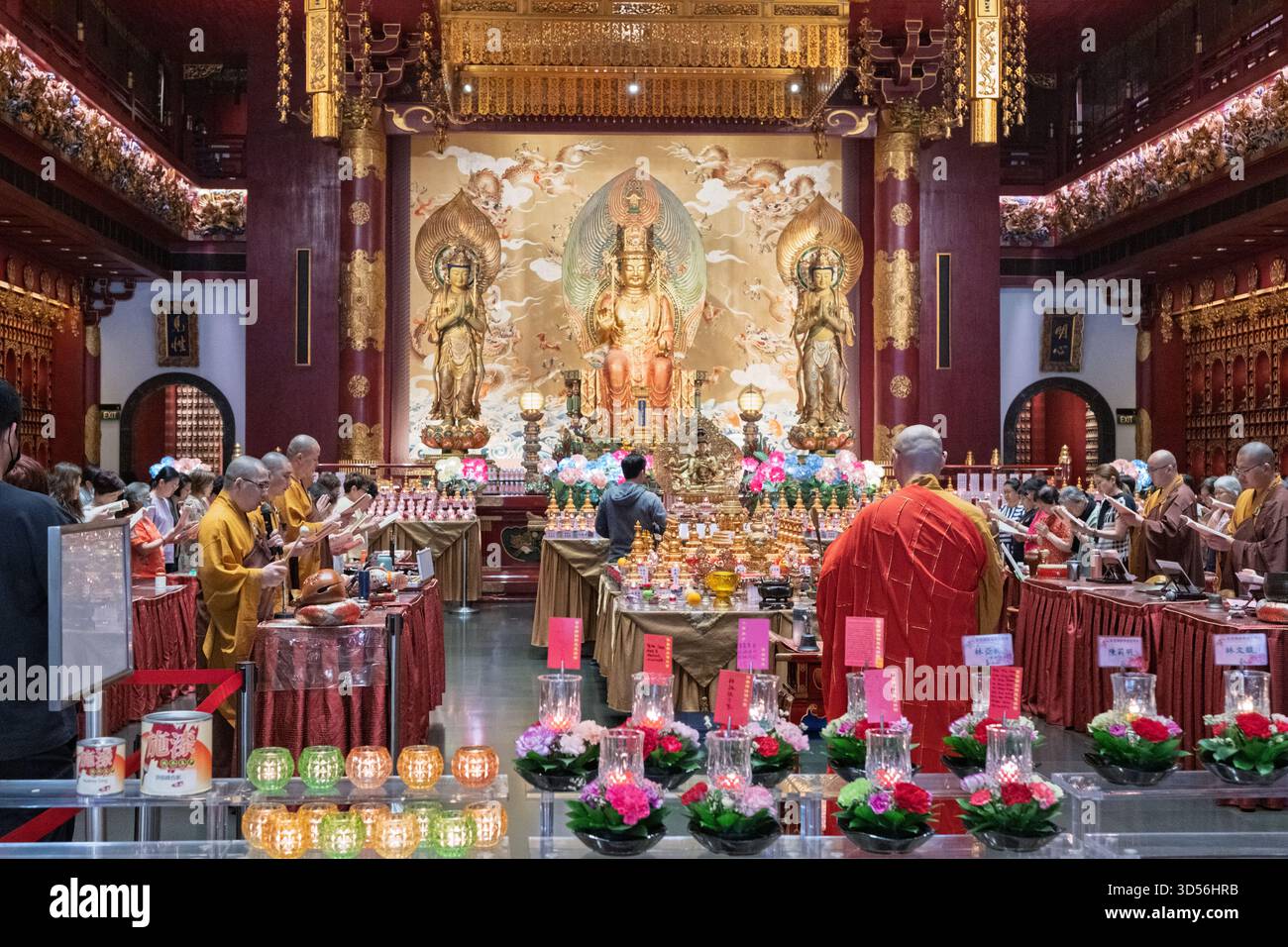 I monaci buddisti conducono una cerimonia di preghiera all'interno del Tempio della reliquia del dente del Buddha a Singapore, circondato da decorazioni ornamentali e offerte rituali. Foto Stock