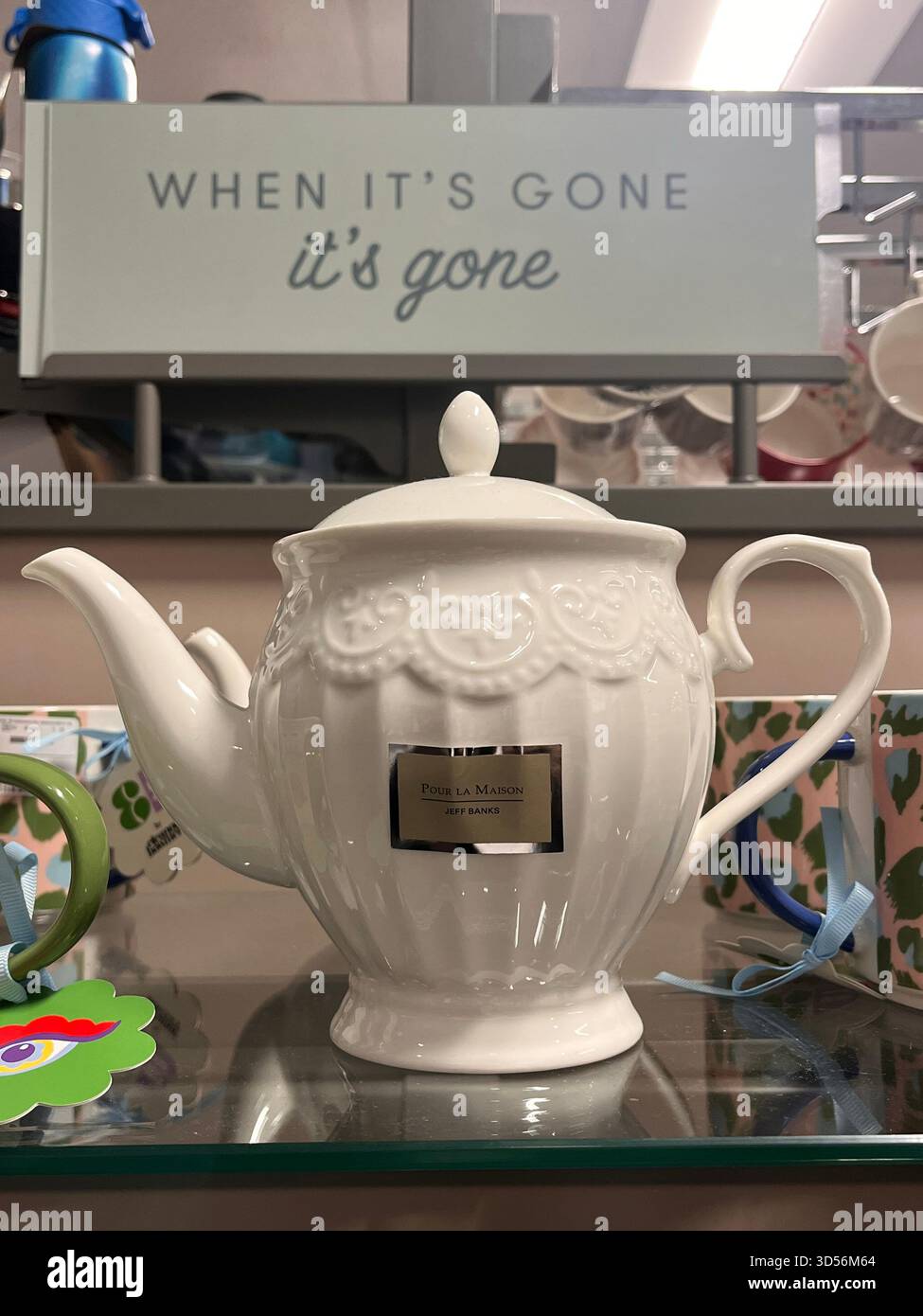 Una teiera decorativa in ceramica bianca esposta sullo scaffale di un negozio a Hull, Inghilterra. L'elegante teiera in stile vintage si trova sotto un cartello con la scritta "When IT" - Immagine stock catturata con smartphone