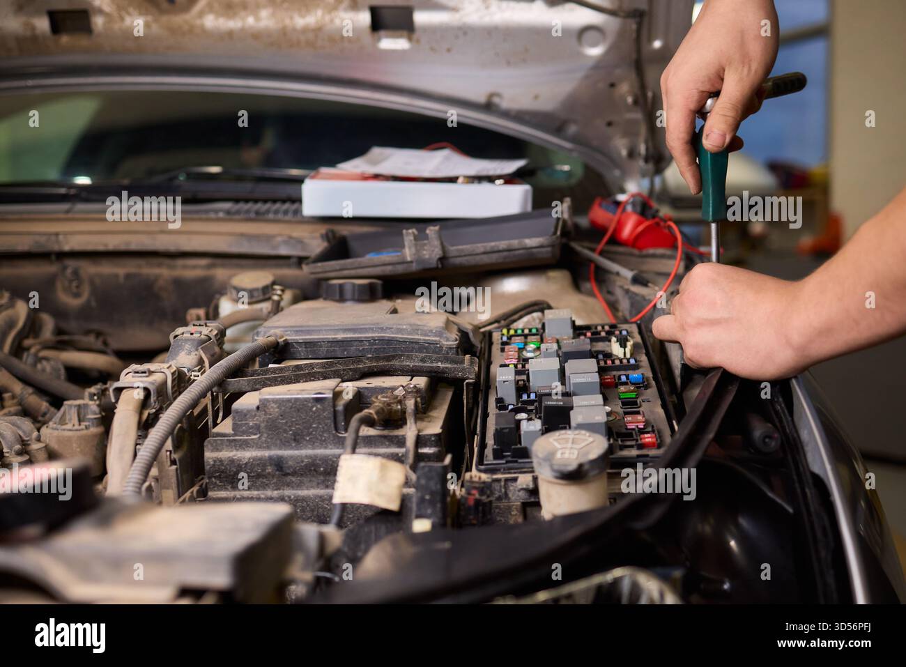 Un tecnico professionista testa con precisione i collegamenti della batteria e del cablaggio, lo specialista del settore automobilistico utilizza un multimetro per valutare e garantire i circuiti del motore Foto Stock