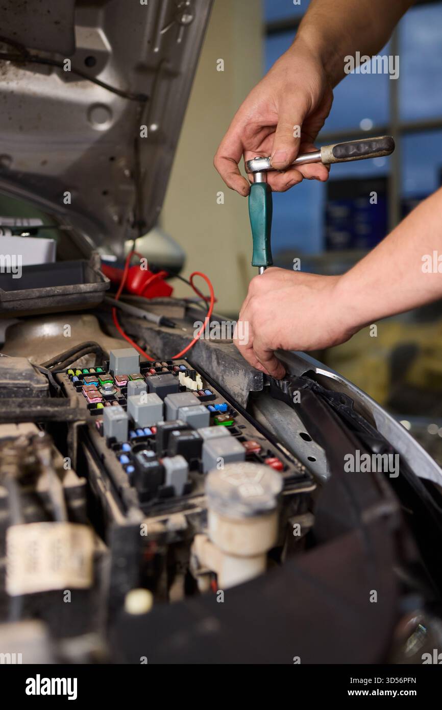 Un tecnico professionista testa con precisione i collegamenti della batteria e del cablaggio, lo specialista del settore automobilistico utilizza un multimetro per valutare e garantire i circuiti del motore Foto Stock