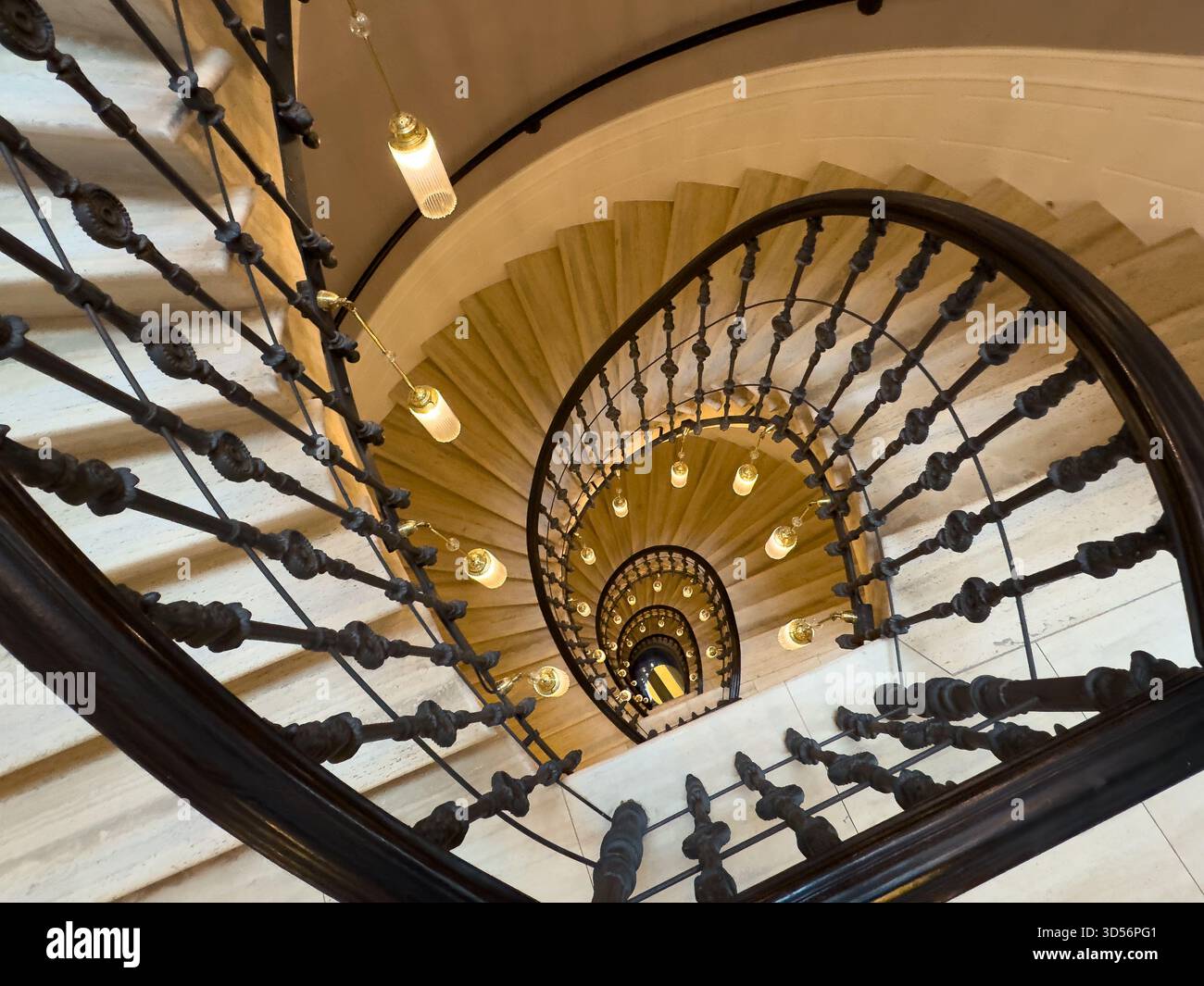 La scala a chiocciola che si snoda verso il basso dall'alto mostra la balaustra in ferro e le luci a sospensione Foto Stock