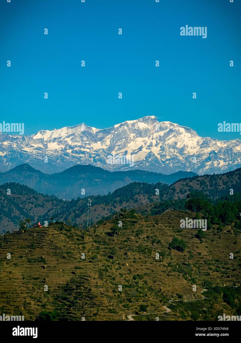 Splendida vista delle montagne himalayane con cime innevate sotto un cielo azzurro. Verdi colline e piccole case di villaggio nella valle creano un paesaggio naturale tranquillo e panoramico. Foto Stock