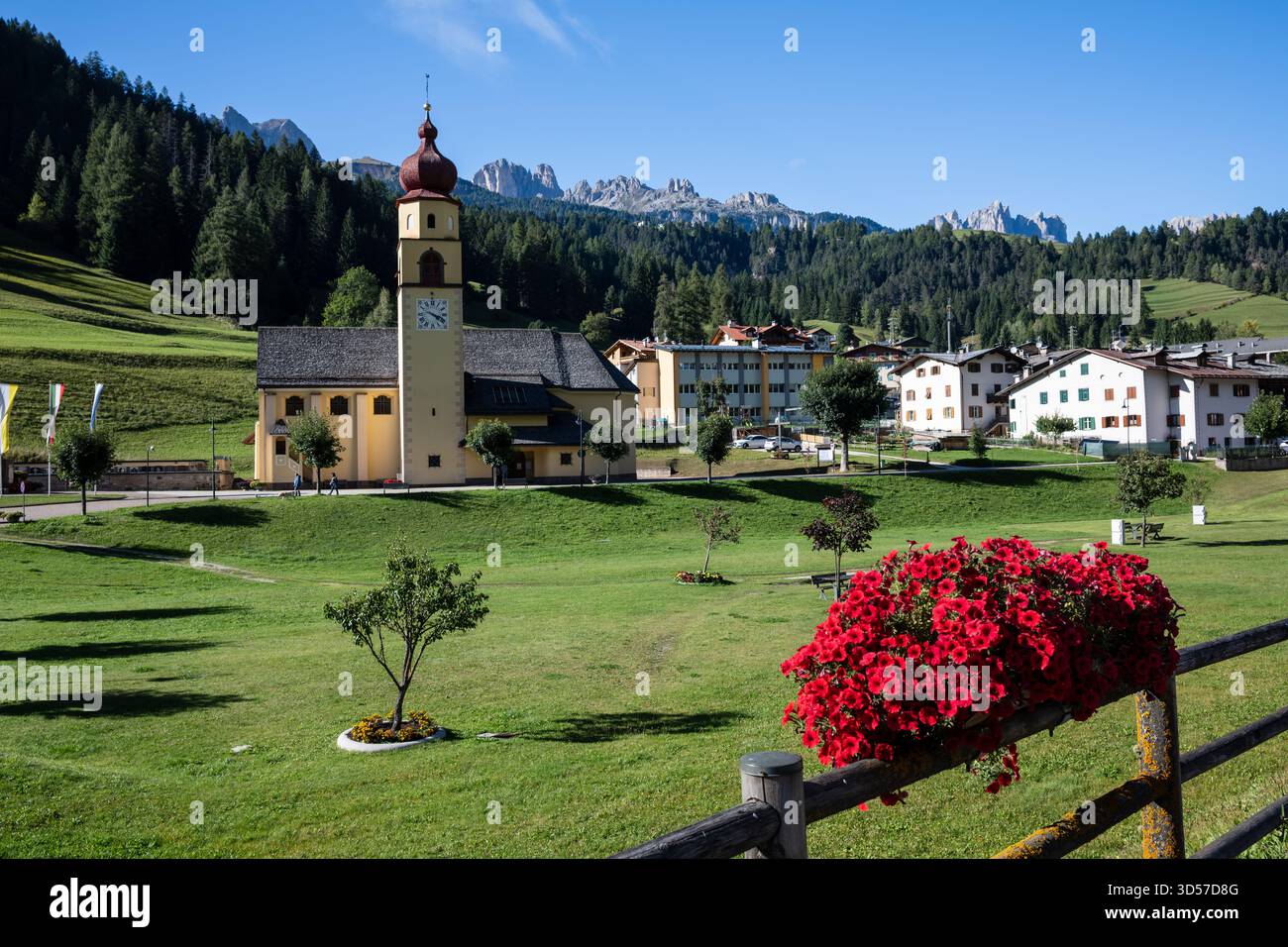 Vista della chiesa a cupola di cipolla a Soraga di Fassa, Trentino alto Adige, Italia con fiori rossi in primo piano Foto Stock