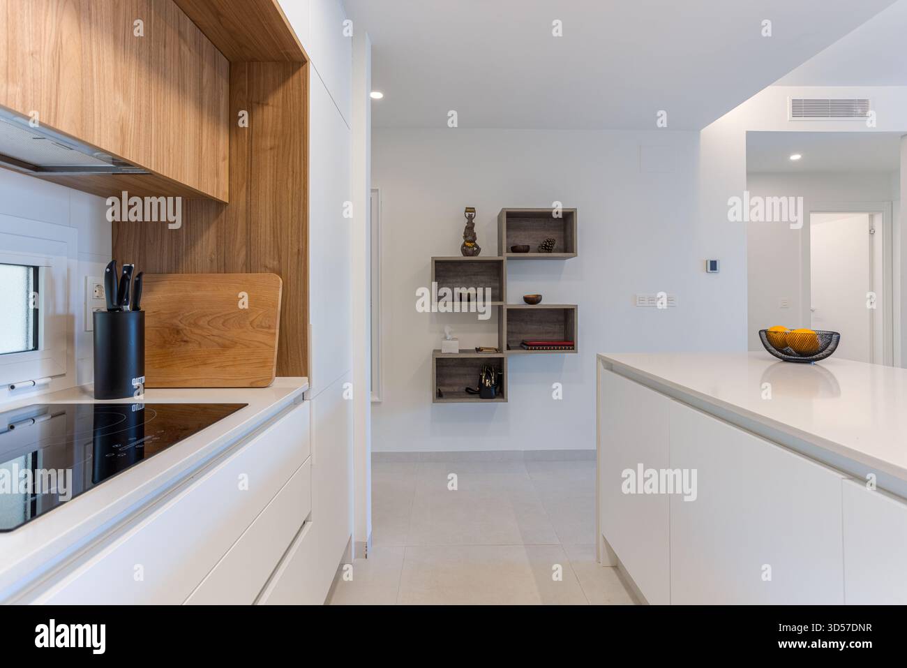 Elegante cucina con mobili bianchi, pannelli in legno, elettrodomestici moderni ed eleganti ripiani aperti contro pareti neutre. Foto Stock