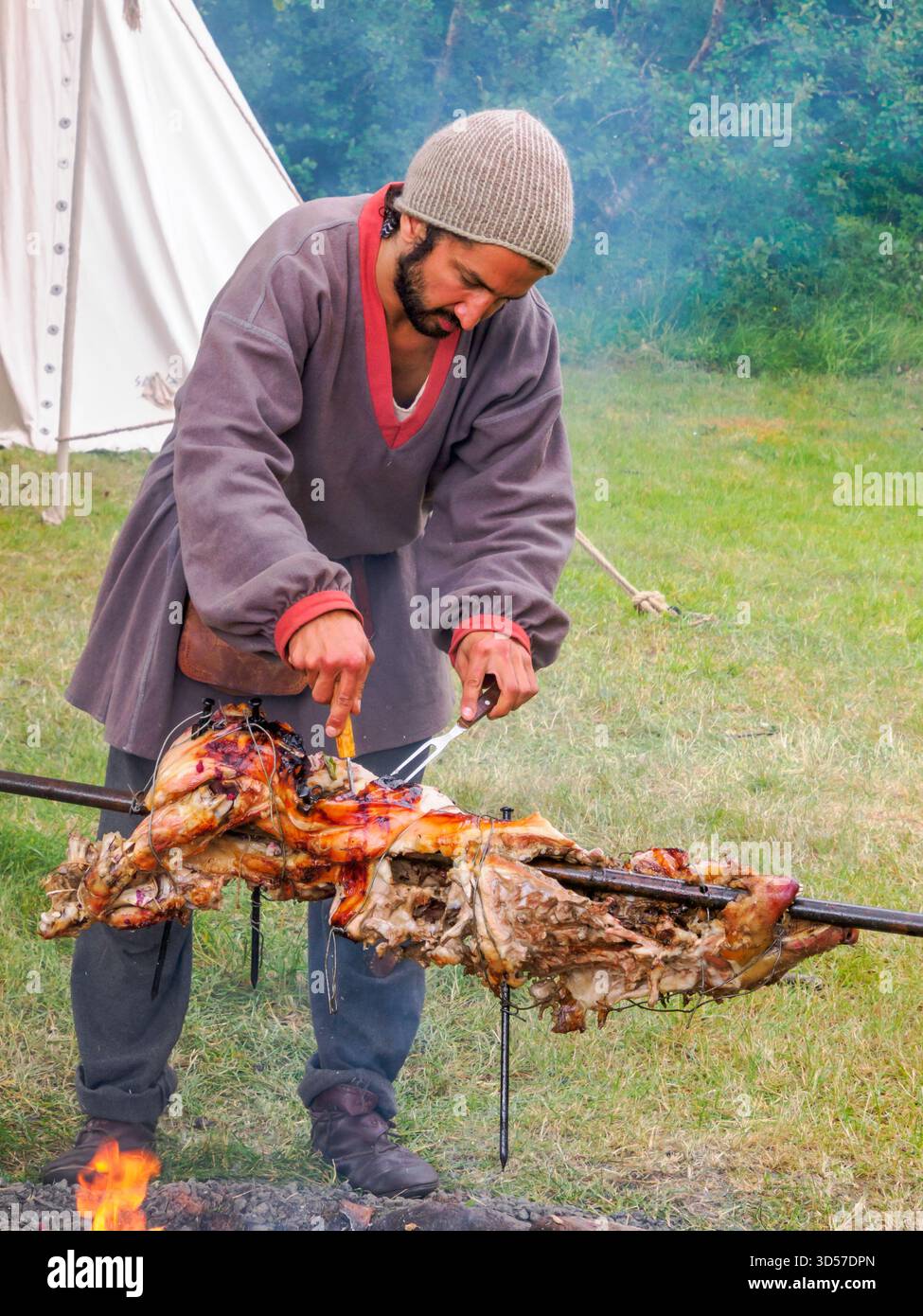 Bøstad, Norvegia - 3 agosto 2023: L'uomo in costumi popolari medievali arrostisce un maiale allo spiedo durante il Festival vichingo presso il Museo vivente dei Vichinghi in Foto Stock