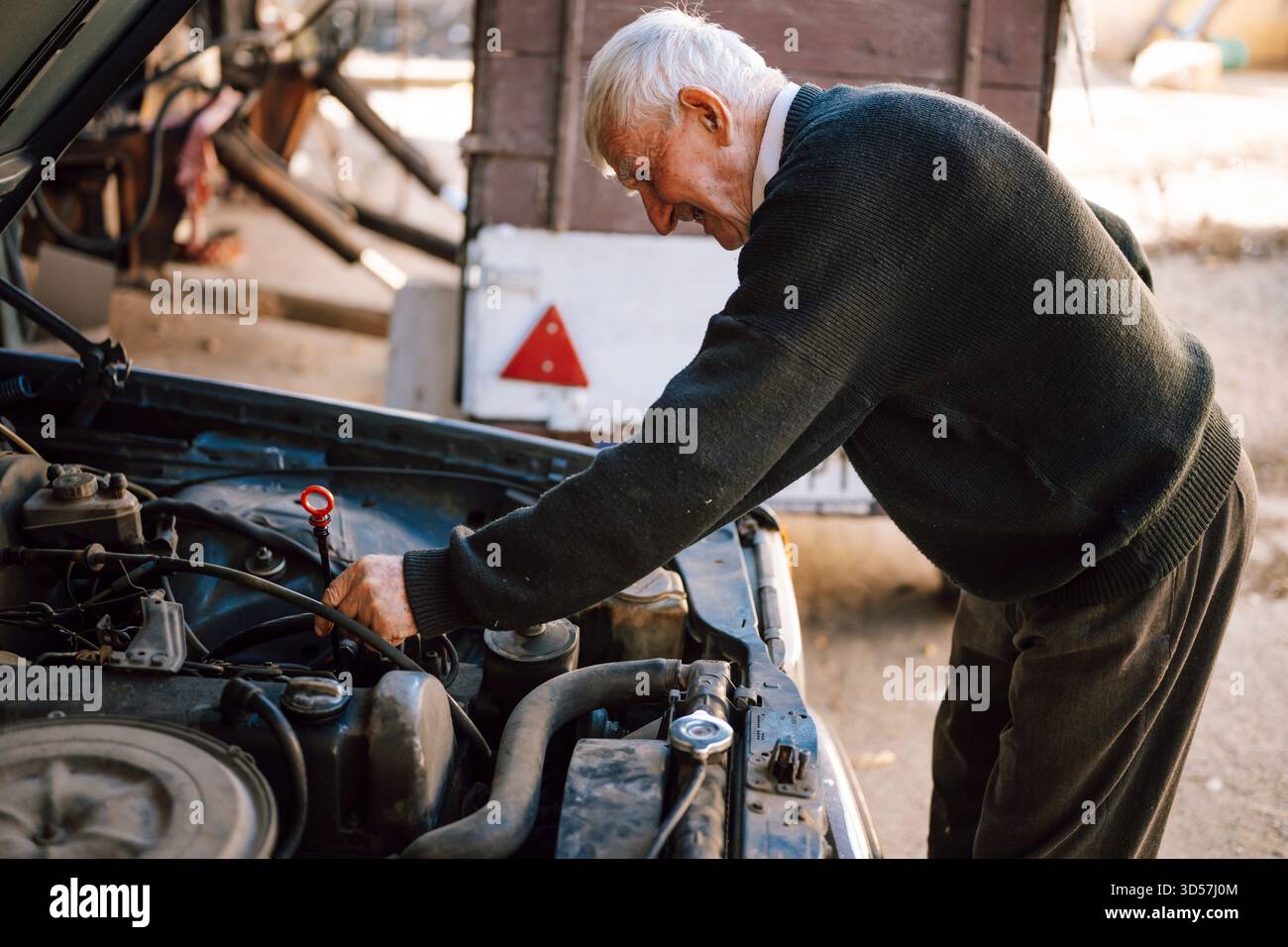 L'uomo anziano ripara il motore dell'auto in un garage rustico Foto Stock