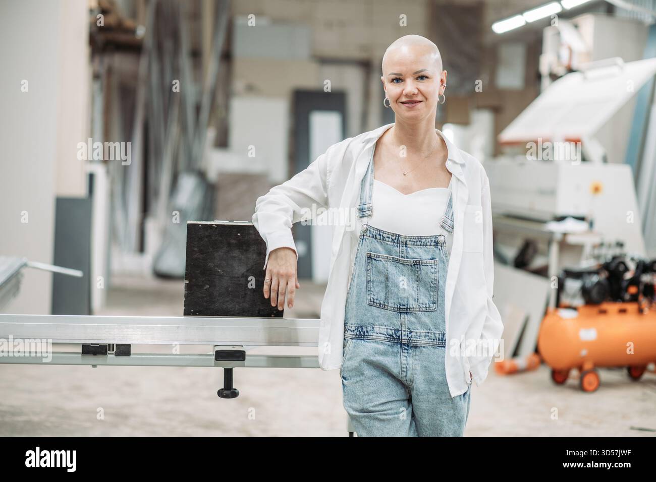 Donna calva in tuta sorridente in falegnameria Foto Stock