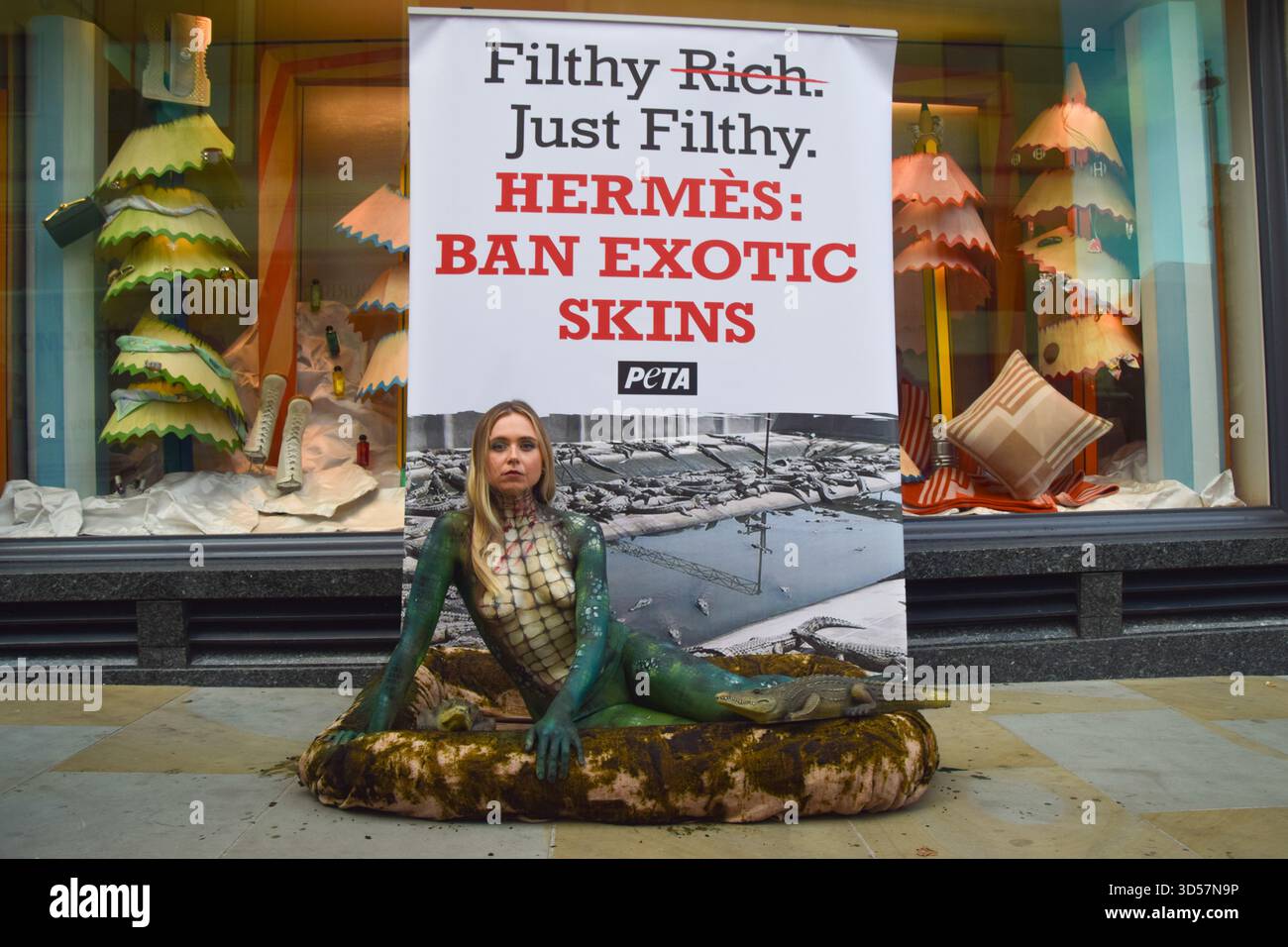 Londra, Inghilterra, Regno Unito. 13 novembre 2025. Un attivista PETA con vernice per il corpo di coccodrillo giace in una piscina "sporca" fuori Hermes in New Bond Street mentre il gruppo per i diritti degli animali organizza una protesta contro l'uso di coccodrilli e altre pelli esotiche da parte del marchio di lusso. (Credit Image: © Vuk Valcic/ZUMA Press Wire) SOLO PER USO EDITORIALE! Non per USO commerciale! Foto Stock