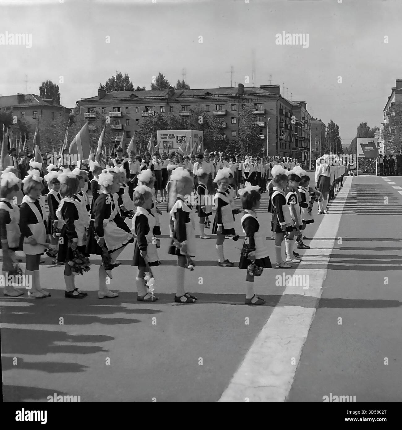 Questa foto archivistica in bianco e nero del 1985 cattura una formazione solenne durante il 40 ° anniversario del giorno della Vittoria (9 maggio) a Sloviansk, RSS Ucraina. Lunghe file di studentesse sovietiche (pioniere) in uniformi scolastiche formali (abiti, grembiuli bianchi, archi) sono all'attenzione, formando un "corridoio vivente" nella Piazza della Rivoluzione d'ottobre (ora Piazza Soborna). Sullo sfondo è visibile una processione con bandiere. Foto Stock