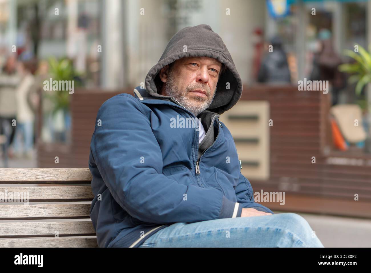 Un uomo in abiti caldi è seduto su una panchina in una strada di città. Foto Stock