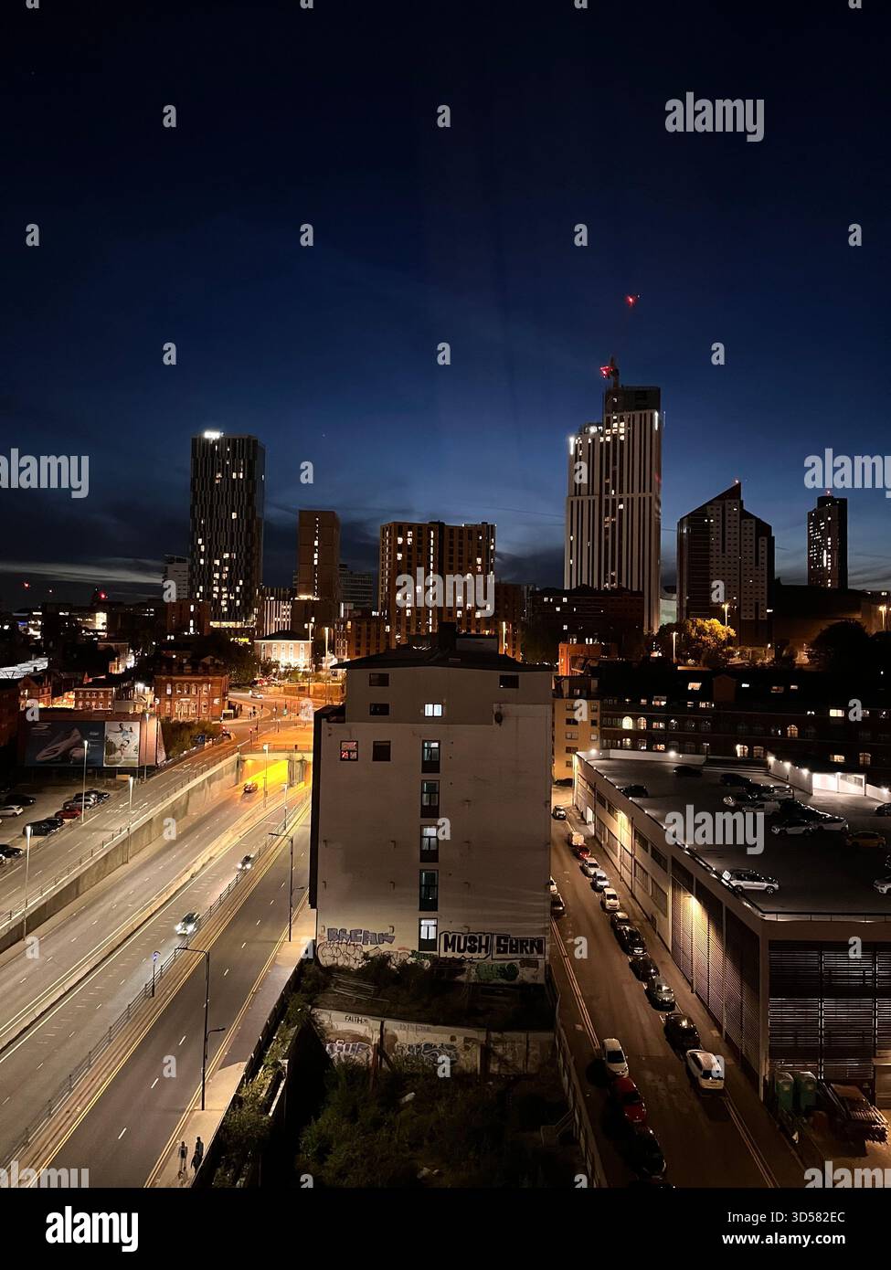 Una vibrante vista notturna di Leeds, Inghilterra, caratterizzata da alti edifici illuminati, una strada trafficata e un cielo blu profondo. Catturato dall'alto Foto Stock