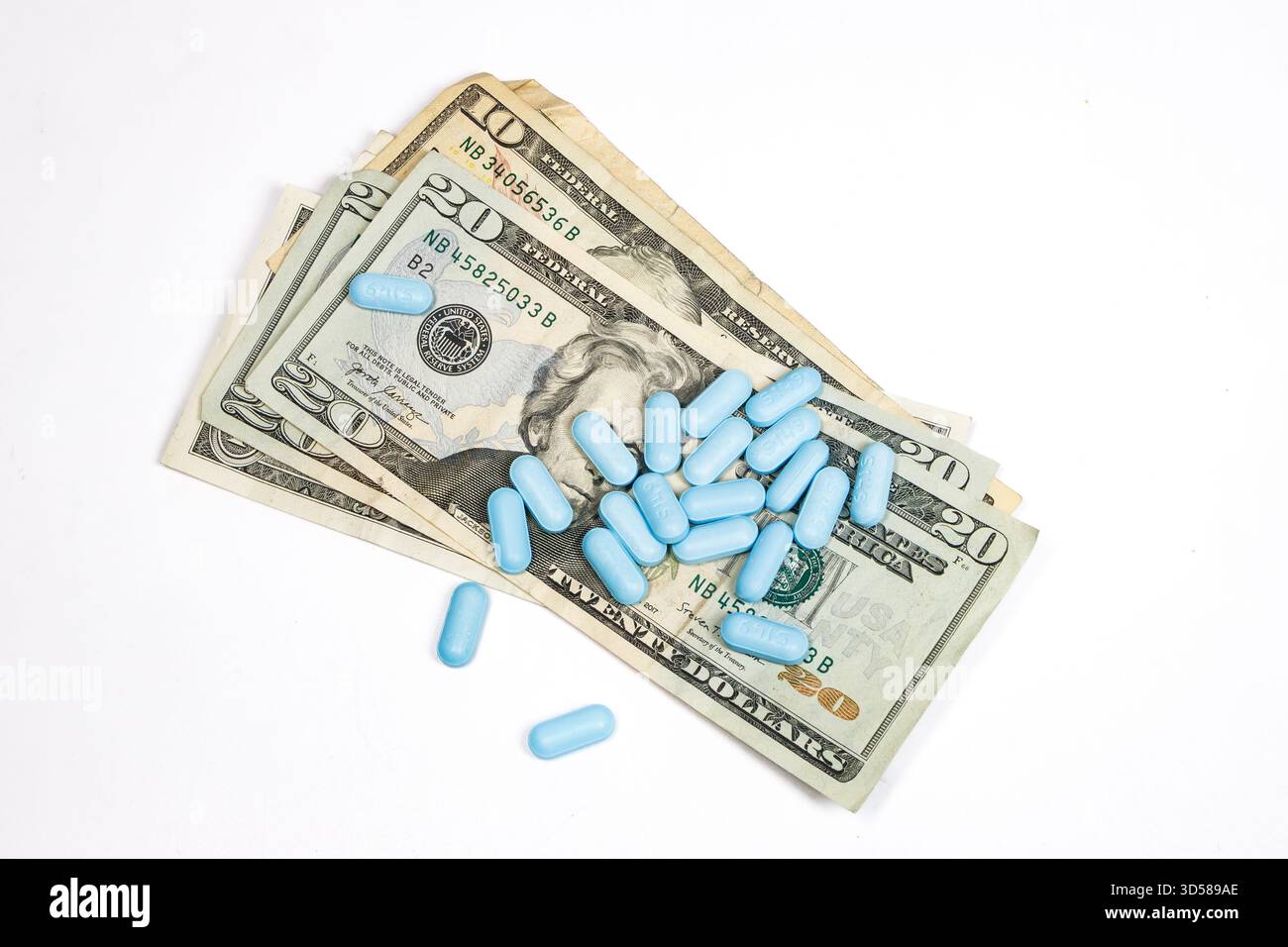 Capsule di medicina blu o pillole sparse su una pila di banconote del dollaro statunitense che simboleggiano il costo delle spese sanitarie o farmaceutiche Foto Stock
