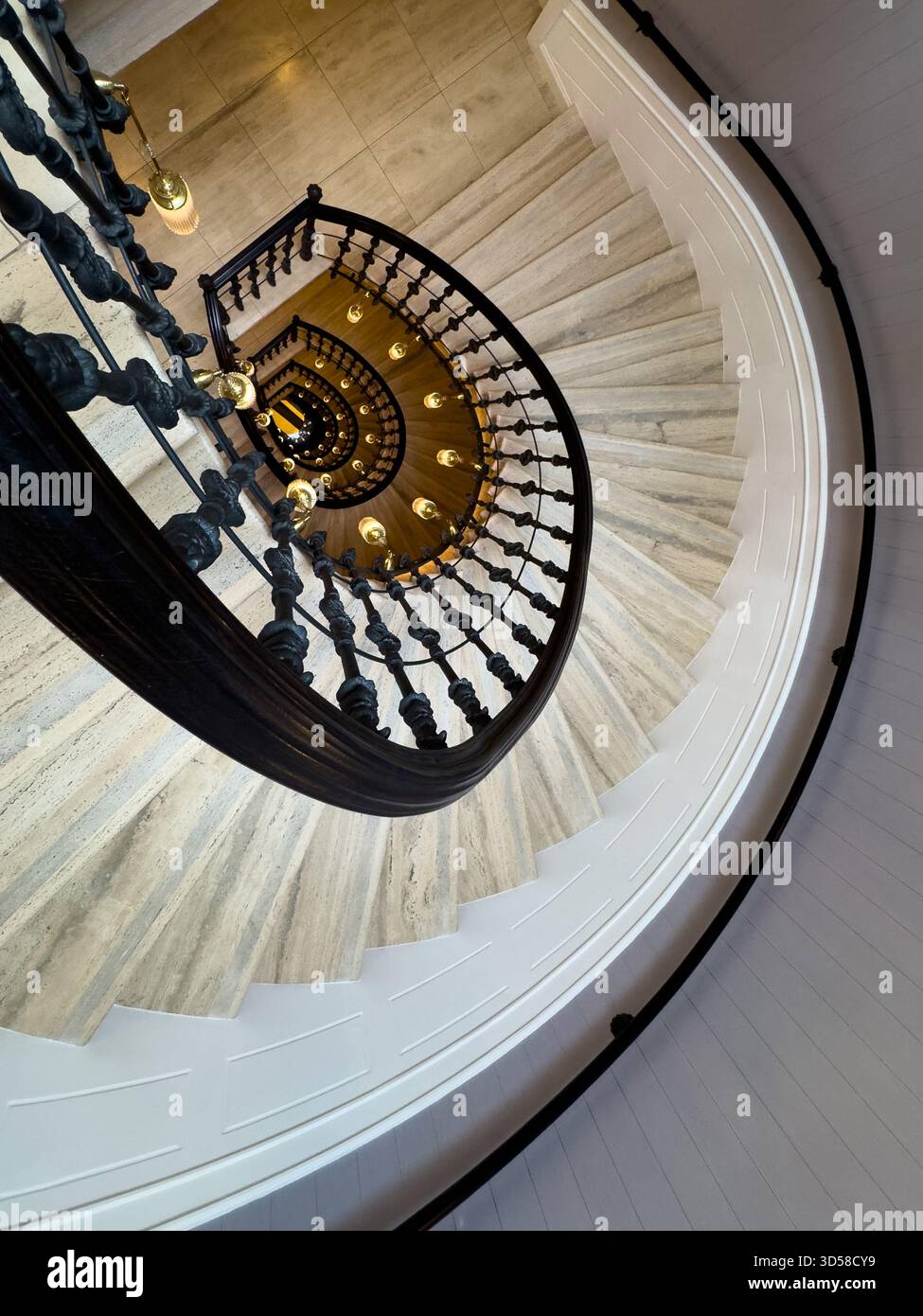 Scala a chiocciola vista dall'alto con ringhiera nera ornata, calde luci a sospensione e gradini in marmo creano un'elegante atmosfera architettonica Foto Stock