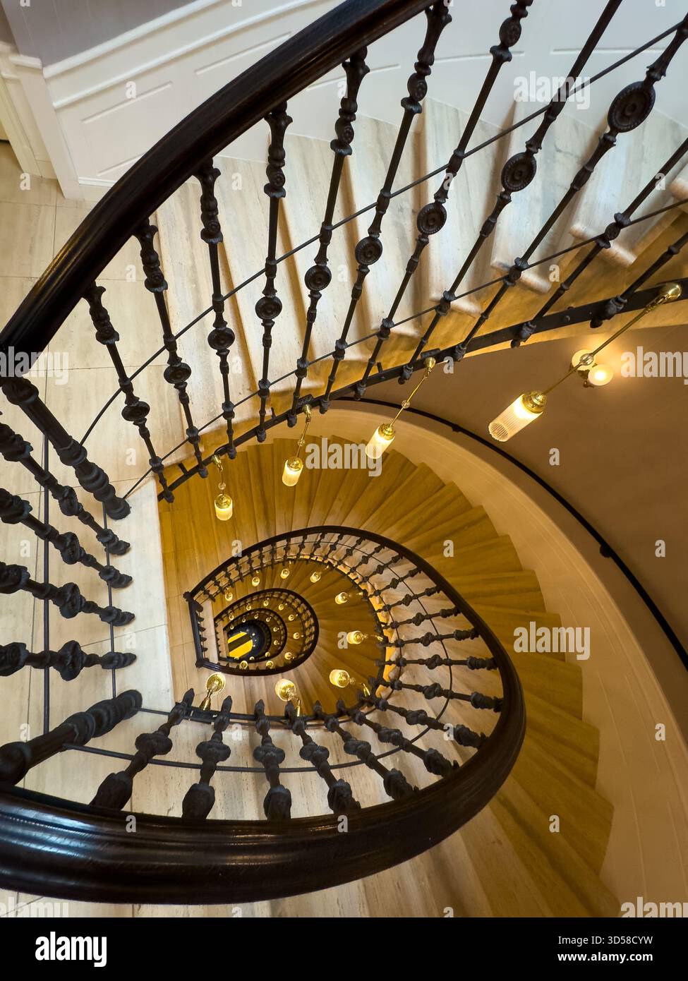 Scala a chiocciola vista dall'alto con ringhiera in ferro battuto gradini in legno e calde luci a sospensione che creano un'invitante atmosfera interna Foto Stock